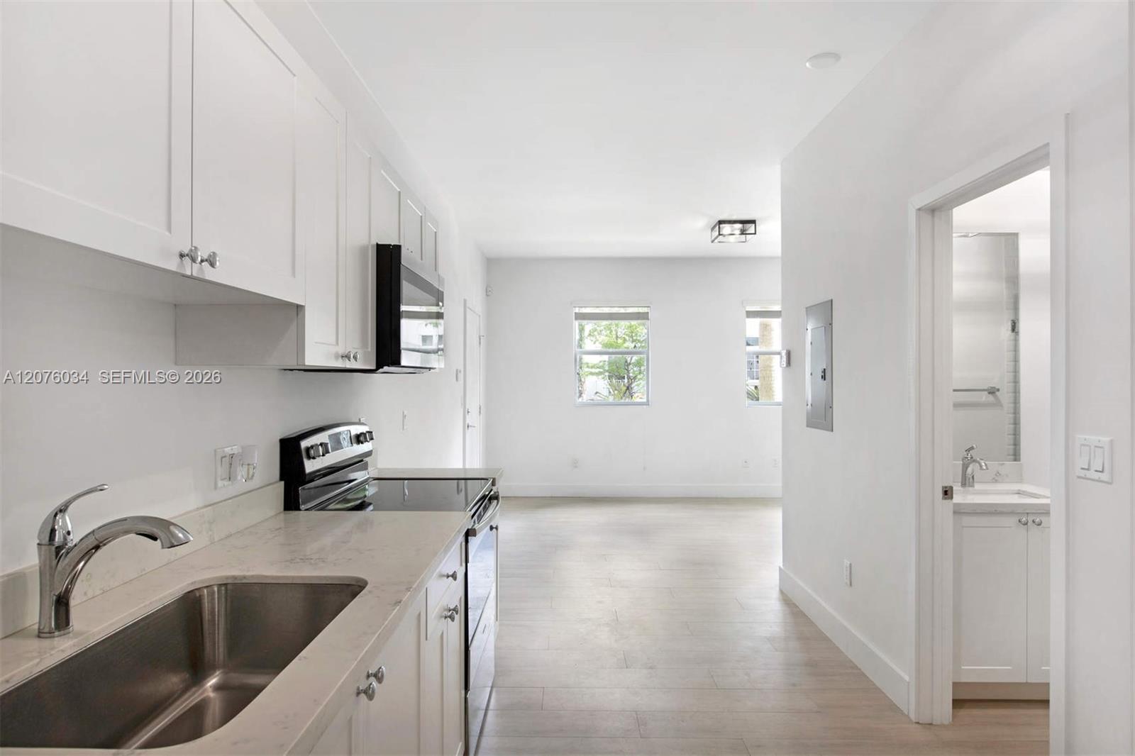 Unfurnished kitchen with white cabinets and stone counters opening into a living area.