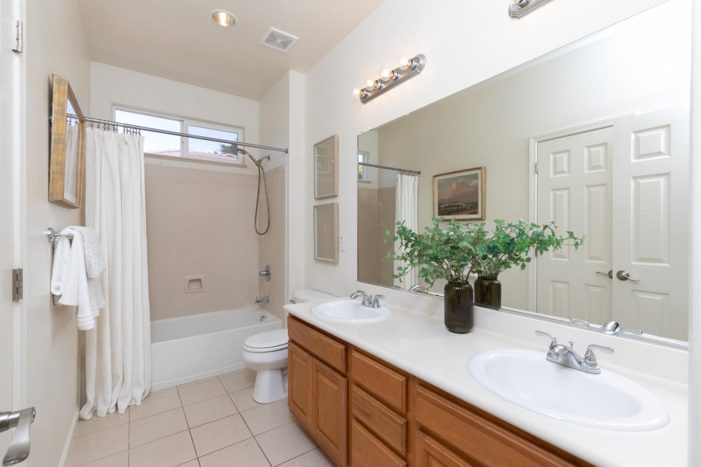 Bathroom with a wood double vanity, large mirror, and curtained bathtub-shower.