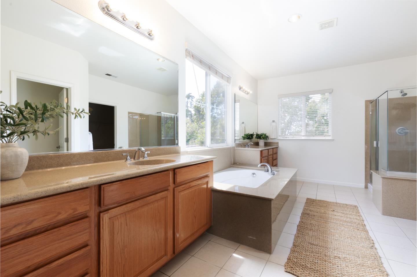 Bright bathroom with a wood vanity, built-in soaking tub, and glass-enclosed shower.