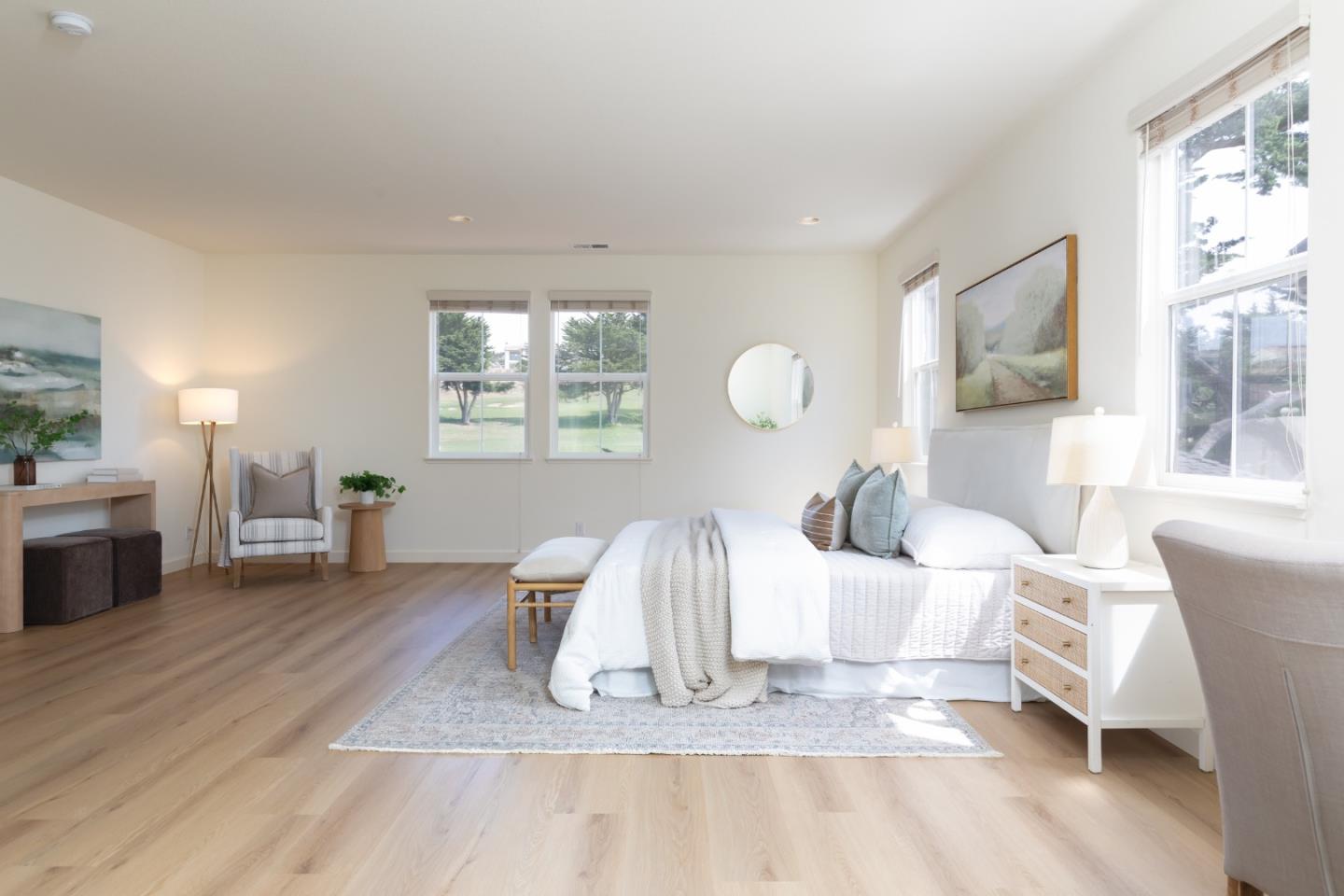 Bright bedroom with a white bed, pale wood floors, and large windows overlooking a green lawn.