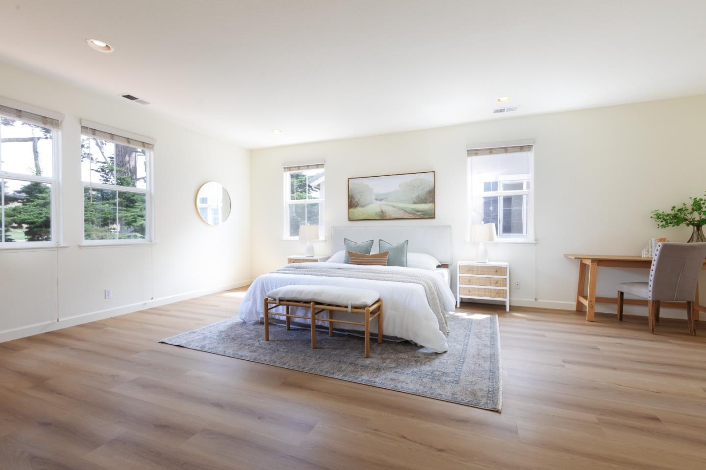 Bright staged bedroom with a white bed, large windows, and light wood floors.
