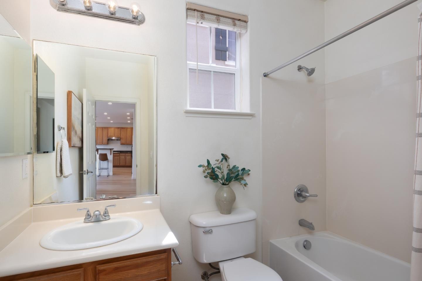 Bathroom with a white tub and shower, wood vanity, and window above the toilet.