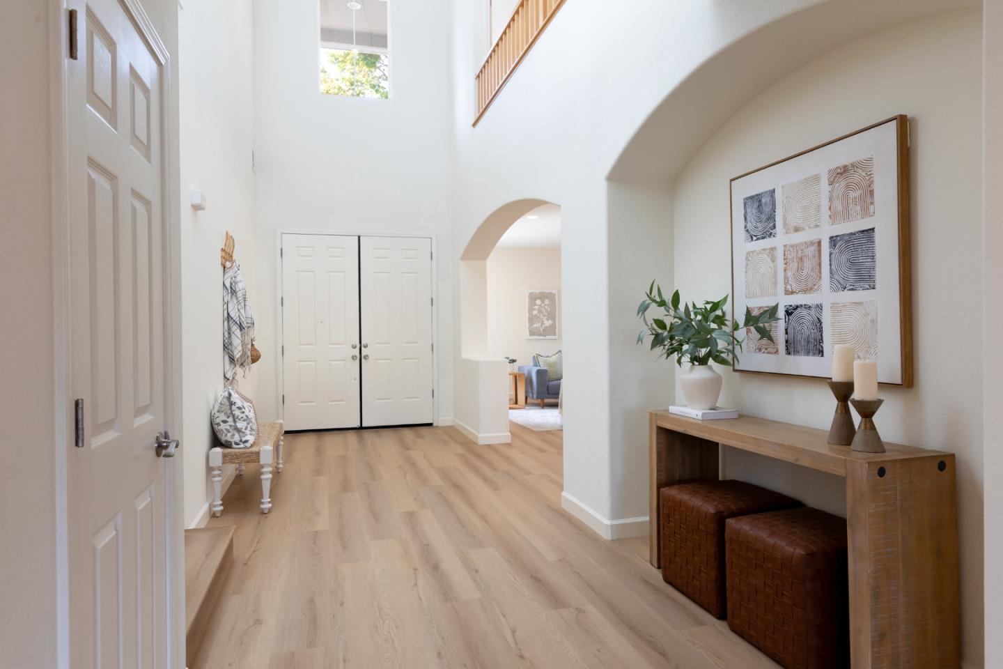 Bright entryway with high ceilings, light wood floors, double doors, and a decorated console table.