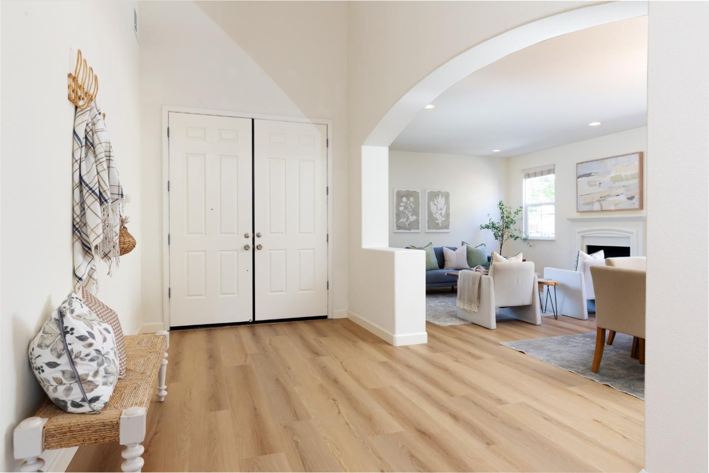 Furnished entryway with white double doors, light wood floors, and an arched opening to the living room.