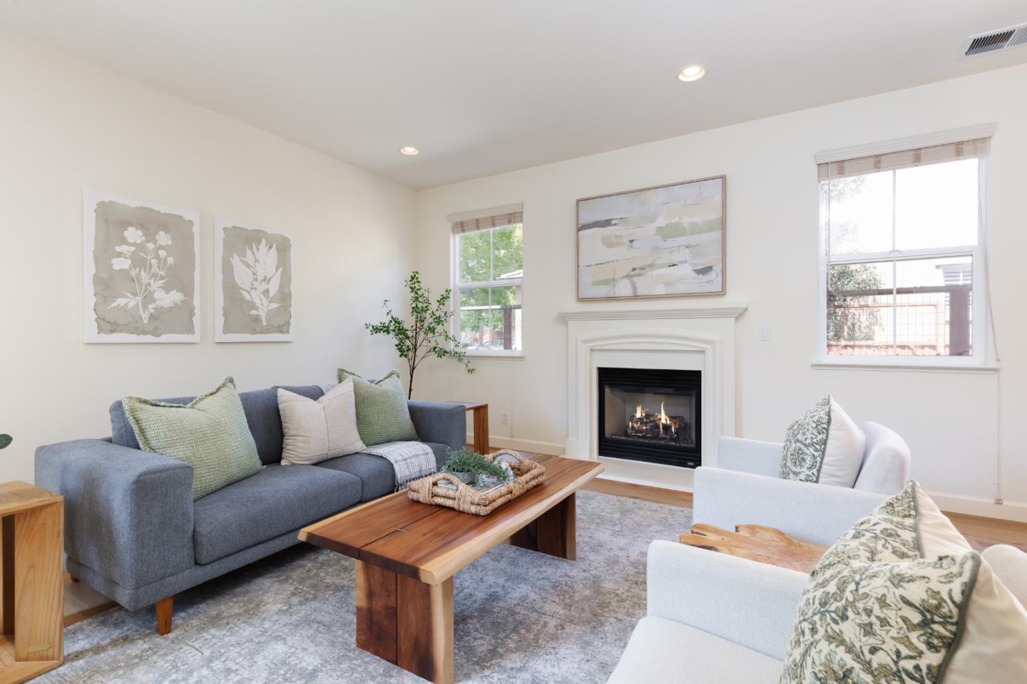 Staged living room with a lit fireplace, gray sofa, white armchairs, and wooden coffee table.