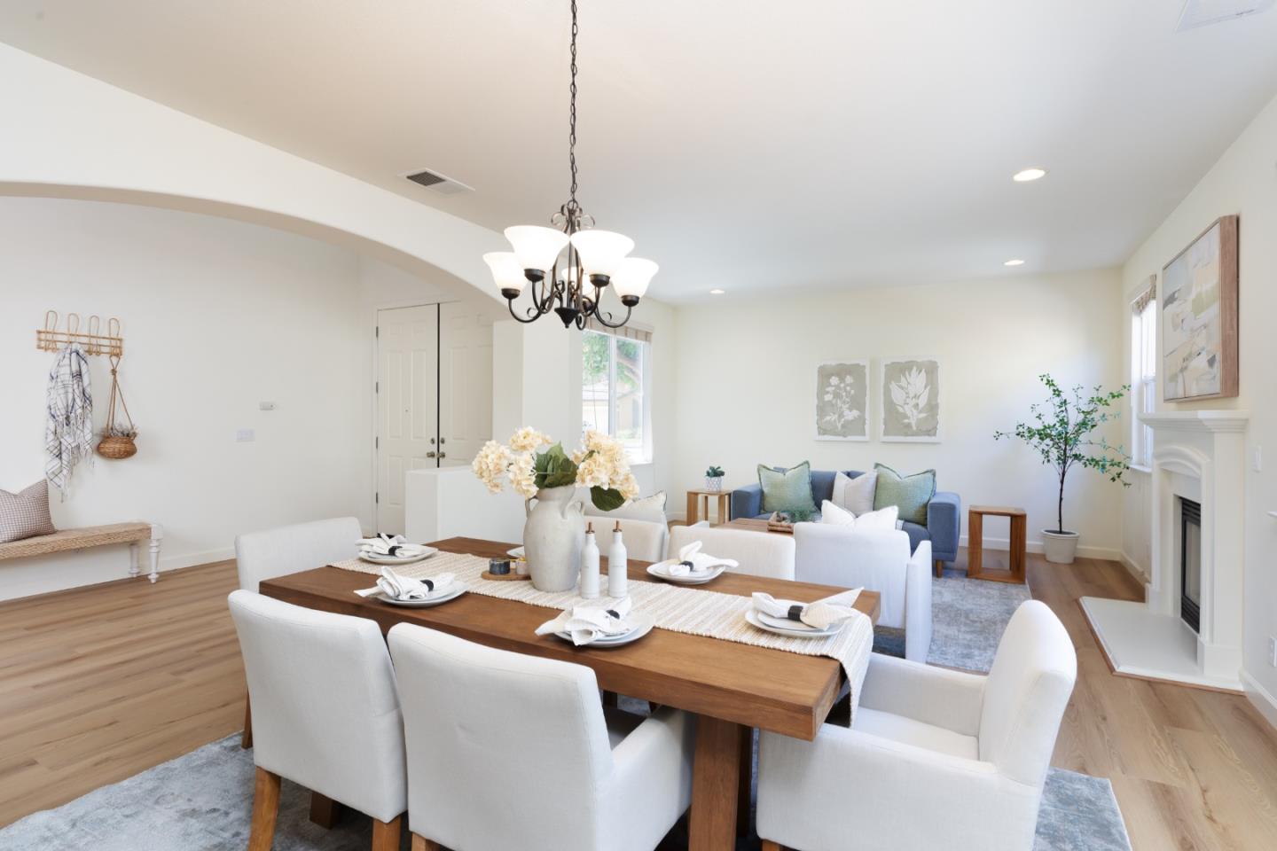 Staged dining and living room with a set wooden table, blue sofa, hardwood floors, and fireplace.