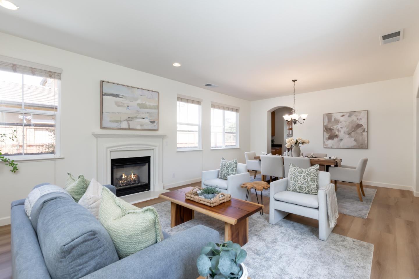 Staged living and dining room with a blue sofa, white armchairs, and a lit fireplace.