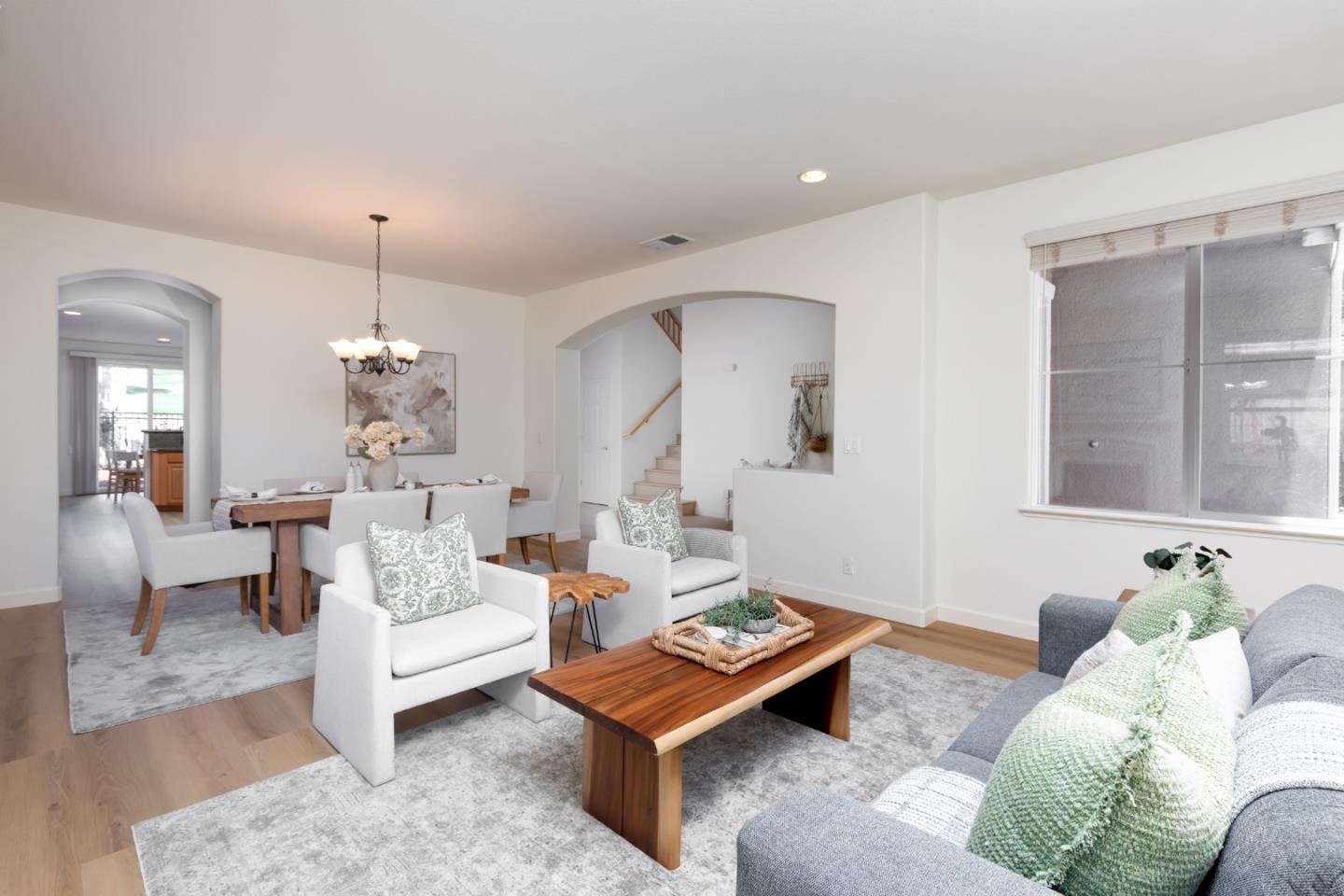 Open-plan living and dining room with a gray sofa, white armchairs, and wood coffee table.