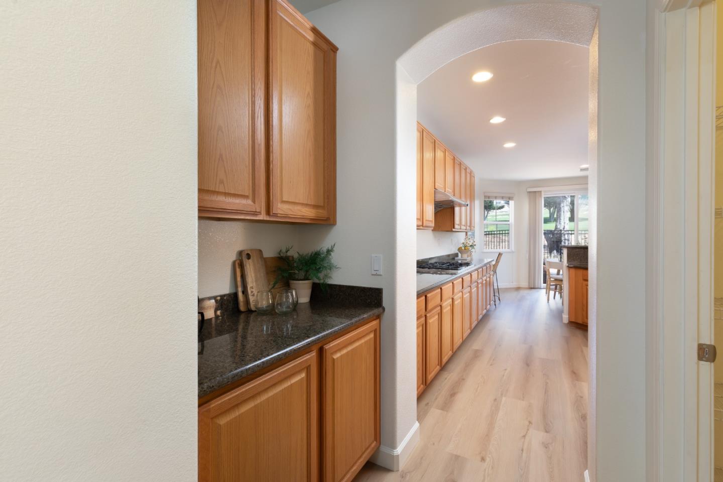 Kitchen with warm wood cabinets and dark countertops, opening toward a dining area and garden view.