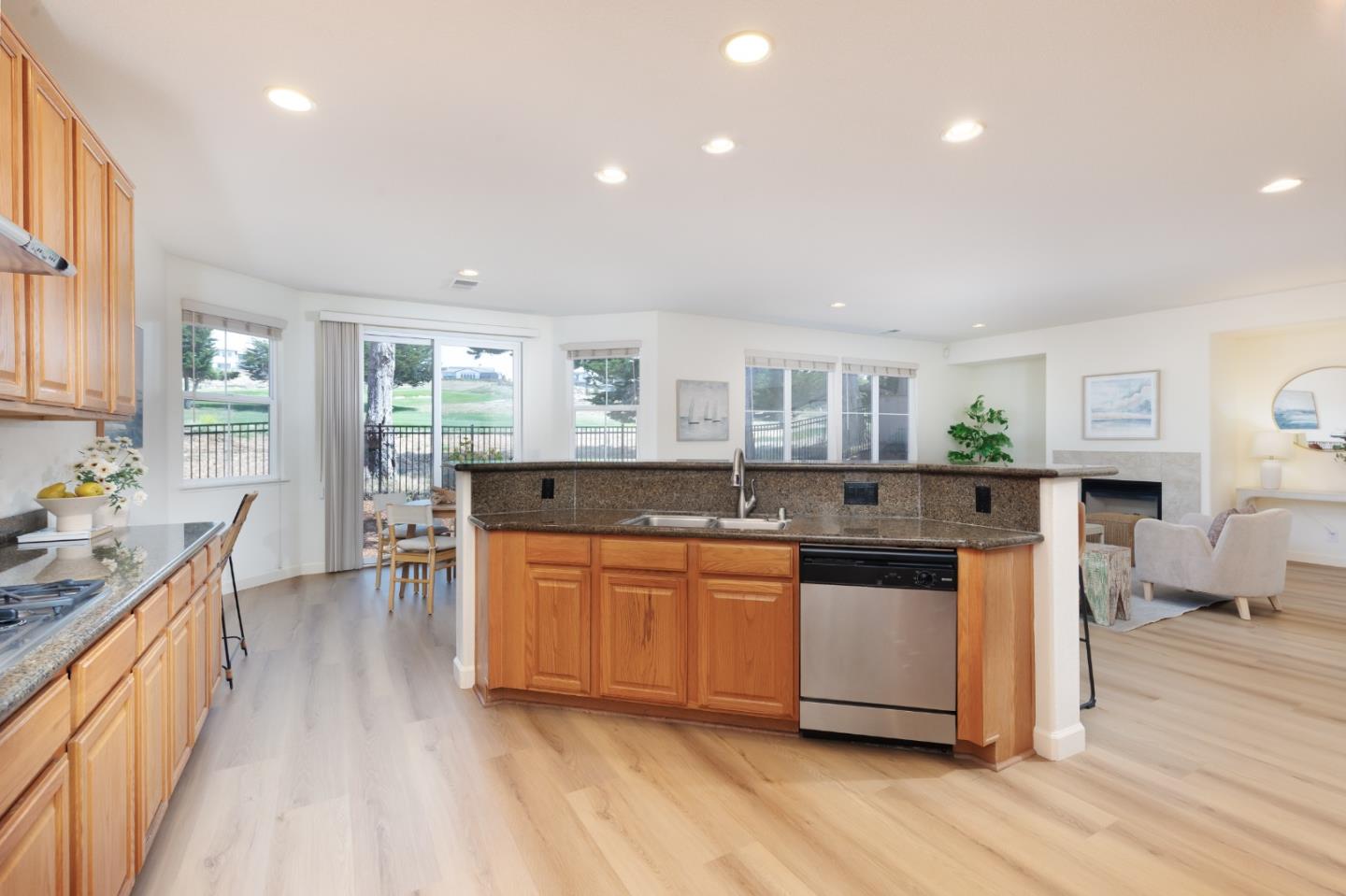 Open kitchen with a granite island, wood cabinets, and large windows overlooking a green lawn.