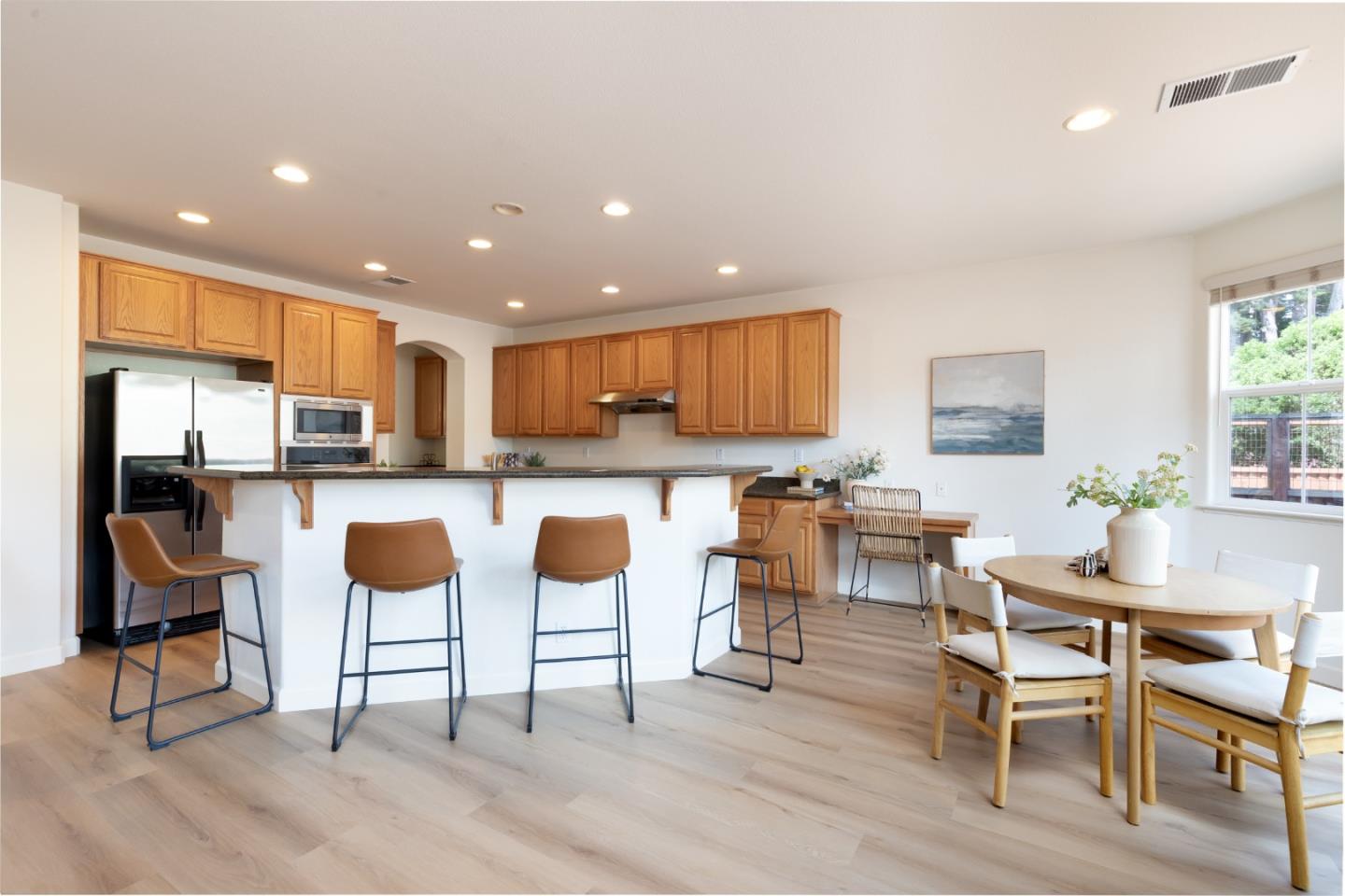 Open kitchen with wood cabinetry, breakfast bar seating, and a dining table by the window.