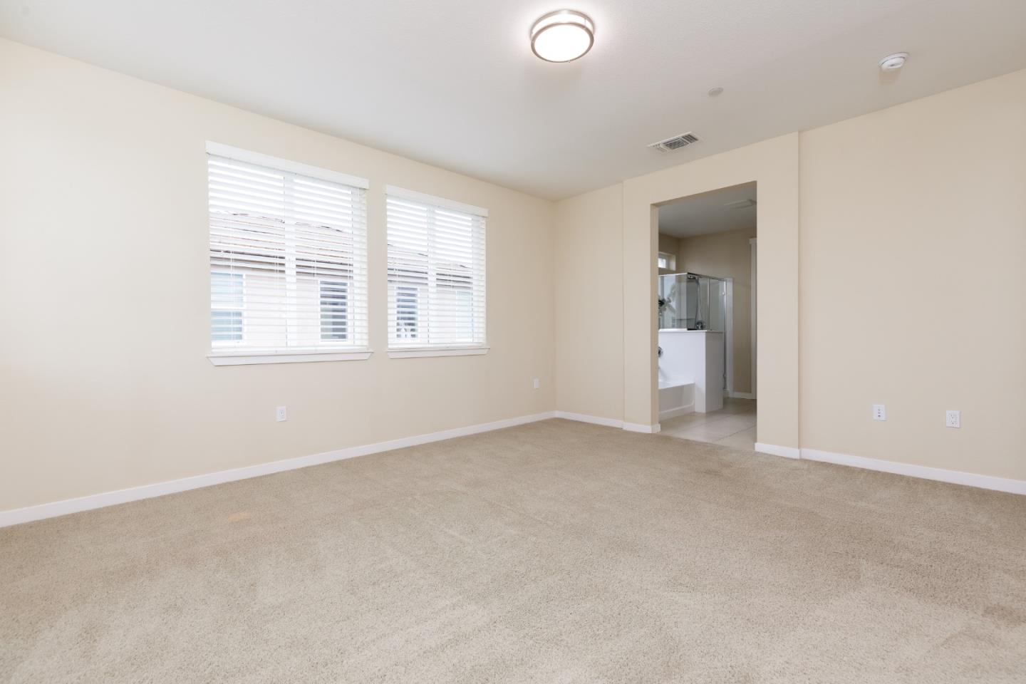 Empty carpeted bedroom with two blinded windows and an open doorway to a bathroom.