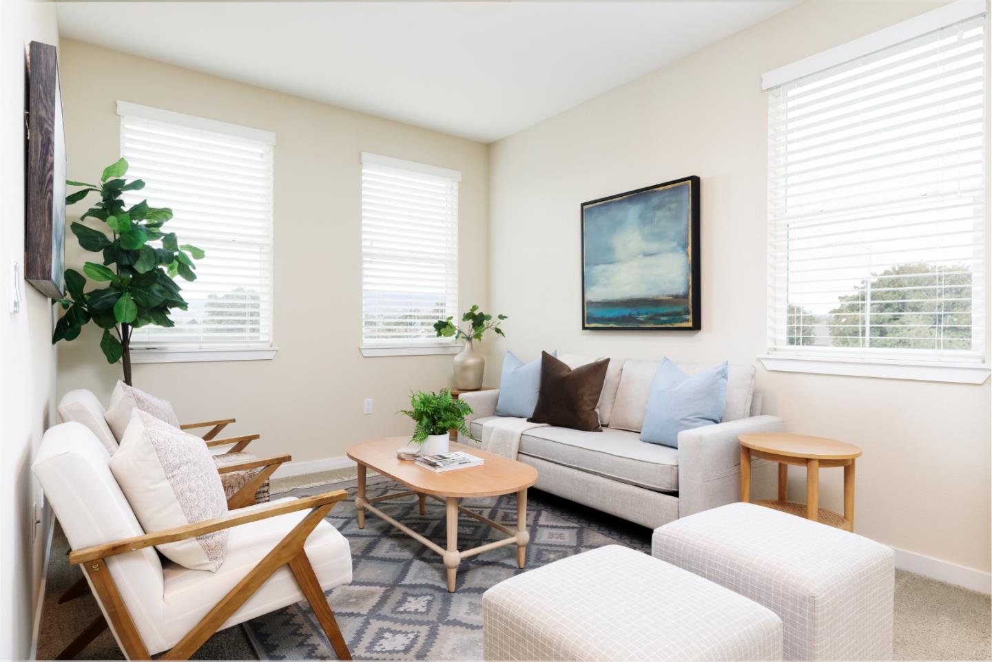 Staged living room with a light sofa, wood-framed chairs, patterned rug, and large windows.