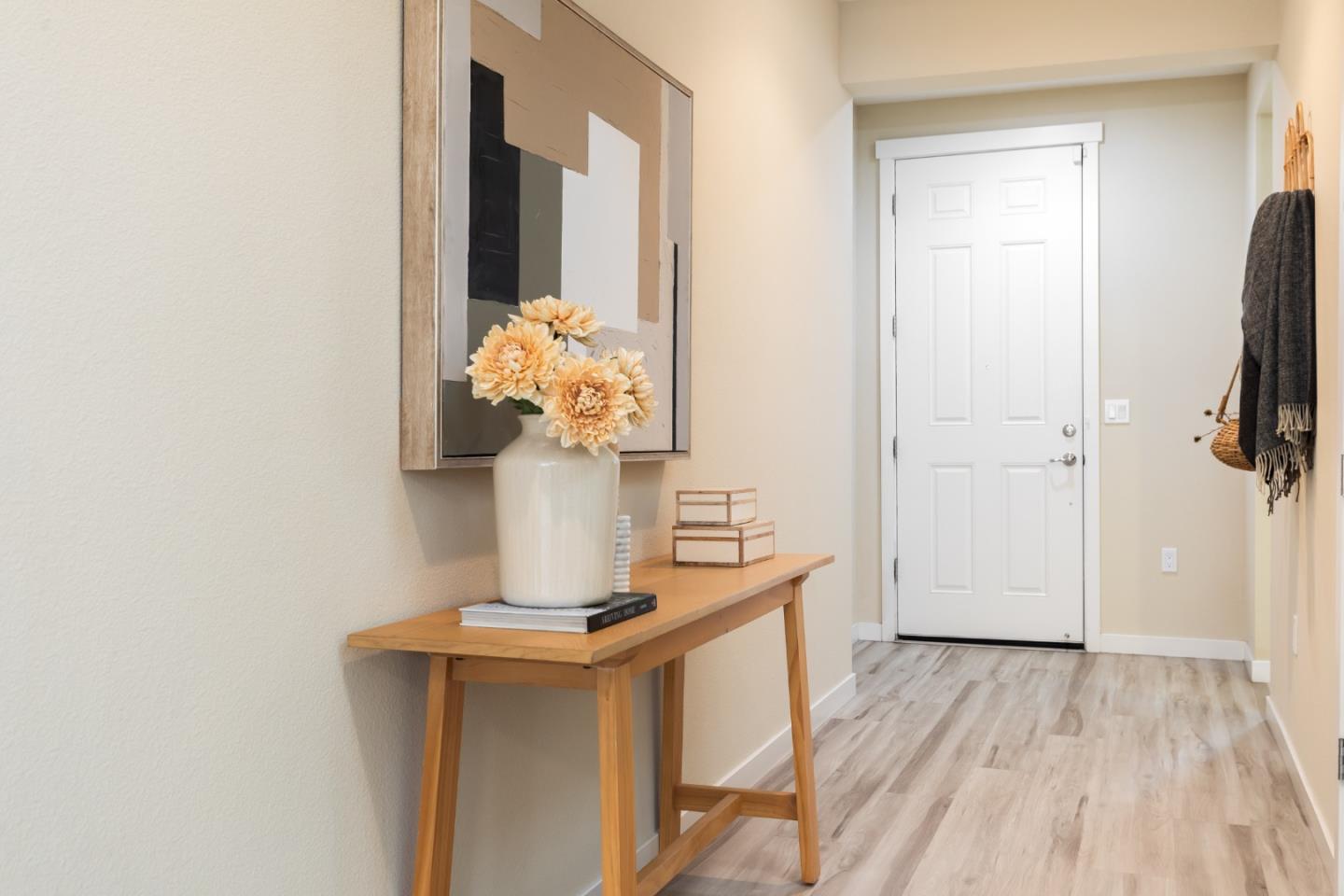 Entry hallway with a white paneled door, wooden console table, flowers, and light wood-look flooring.