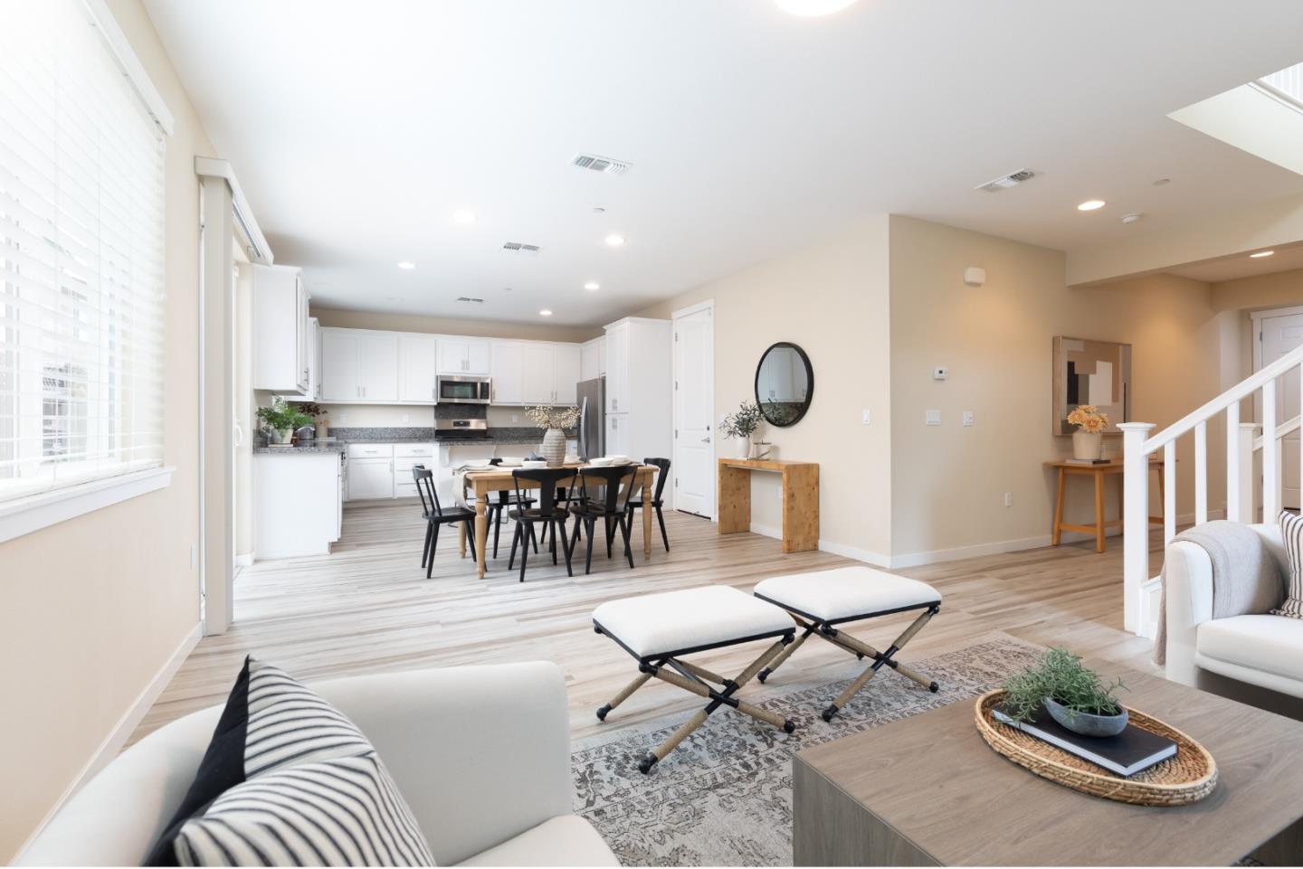 Open-plan living room, dining area, and white kitchen with light wood-look floors and neutral furnishings.