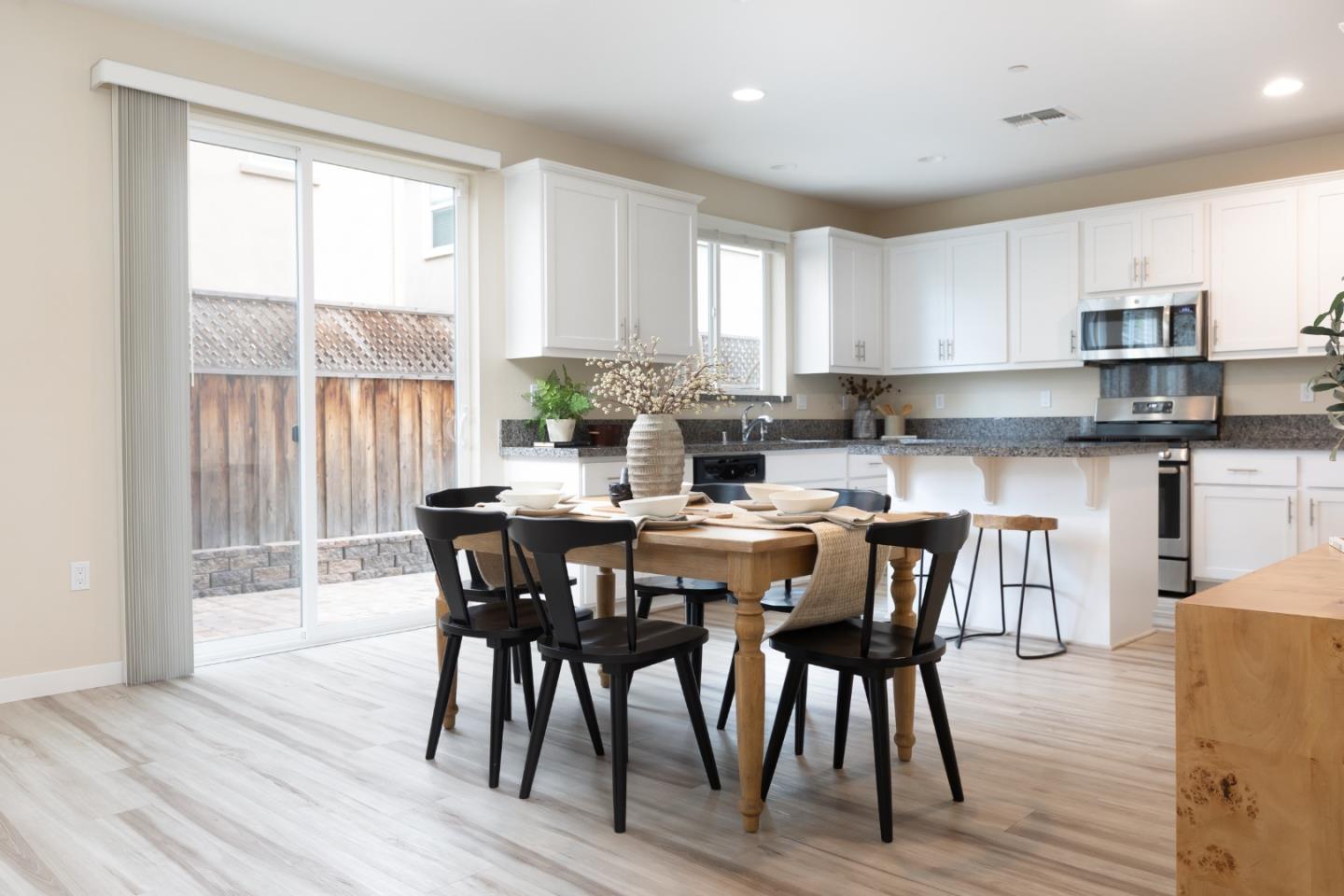Open kitchen and dining area with white cabinets, granite counters, and a set table beside sliding glass doors.