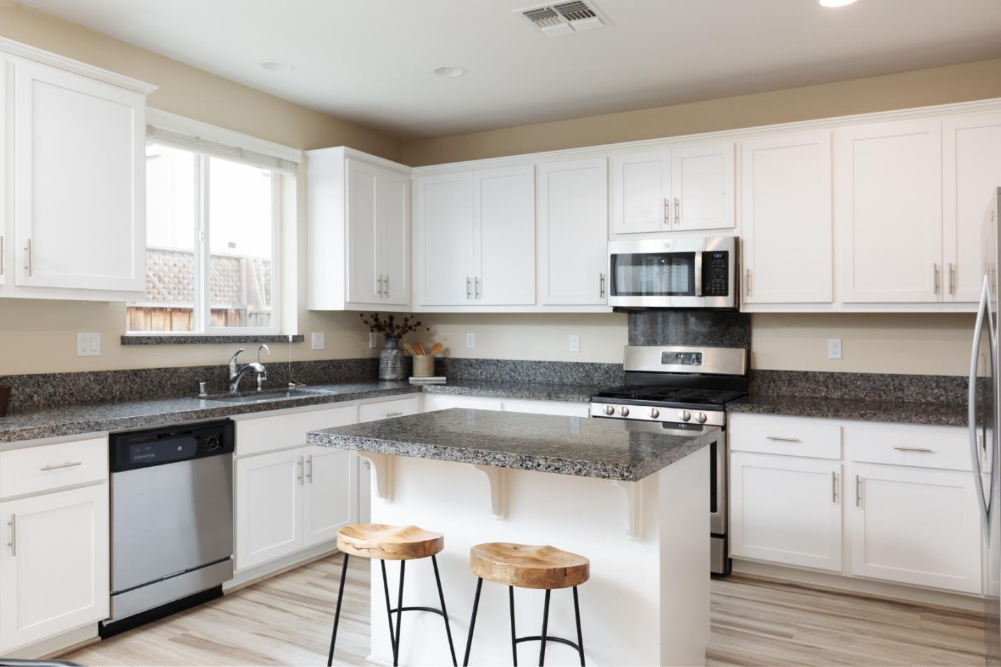 Kitchen with white cabinets, granite counters, a central island, and stainless steel appliances.