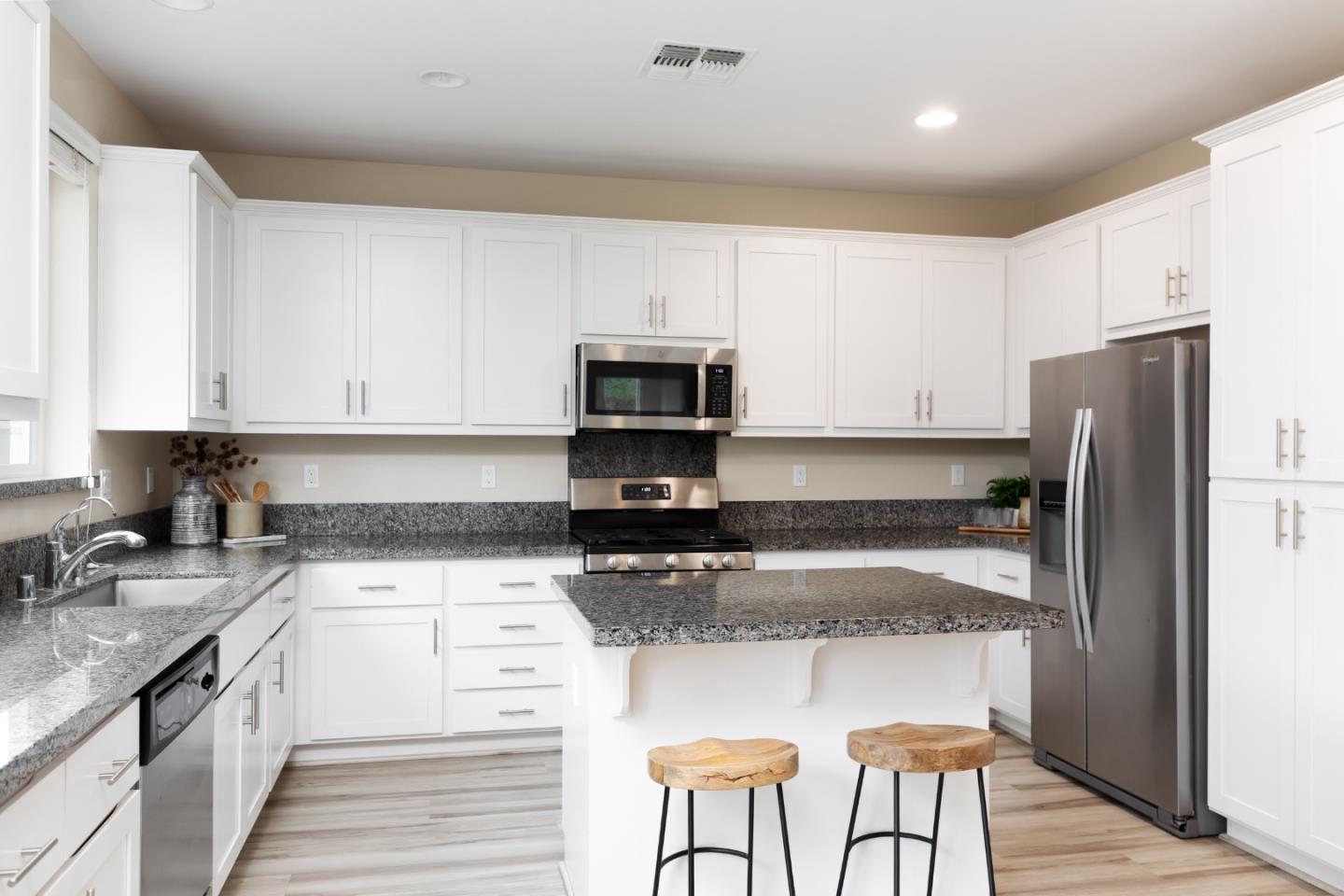 Kitchen with white cabinets, granite island, two stools and stainless steel appliances.