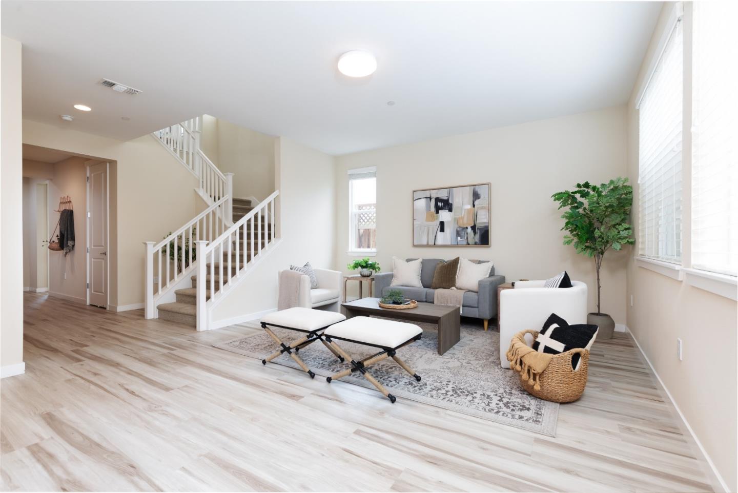 Staged living room with a gray sofa, white armchairs, large windows, and an open staircase.