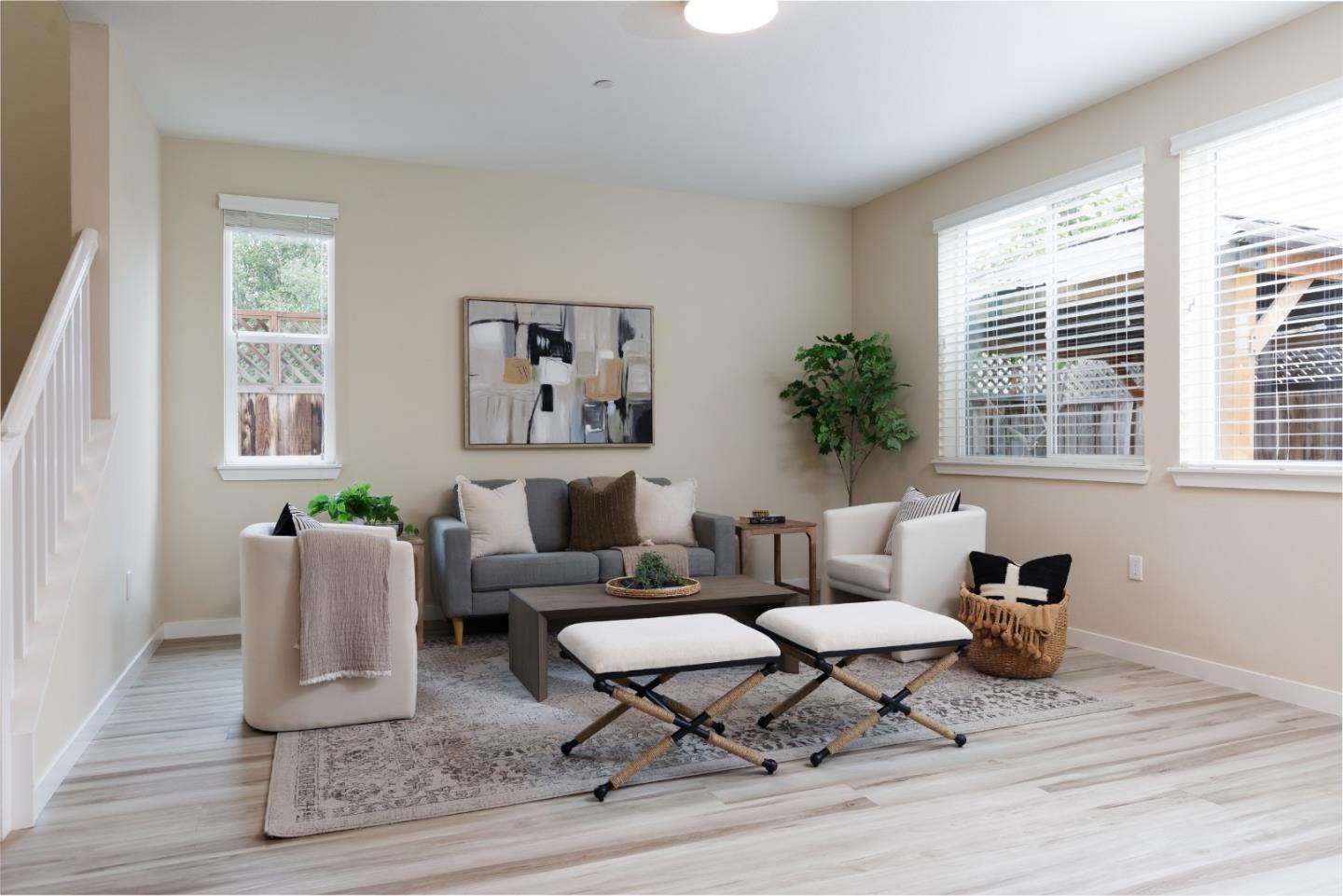 Staged living room with a gray sofa, white chairs, large windows, and light wood floors.