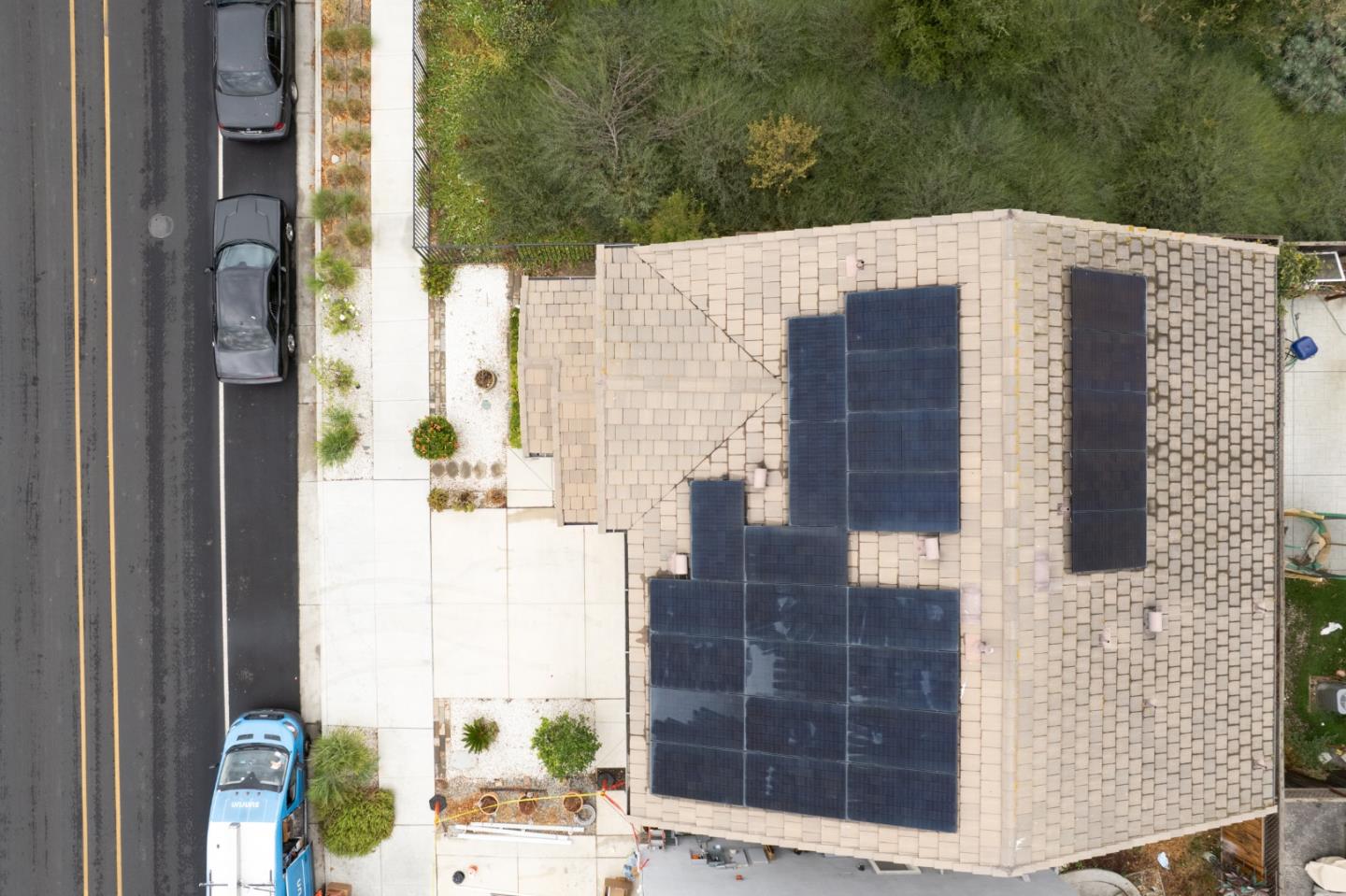 Aerial view of a tiled home roof covered with solar panels beside a street.