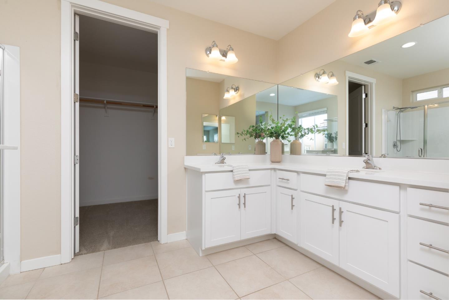 Bathroom with a white double vanity, broad mirrors, and an open walk-in closet.