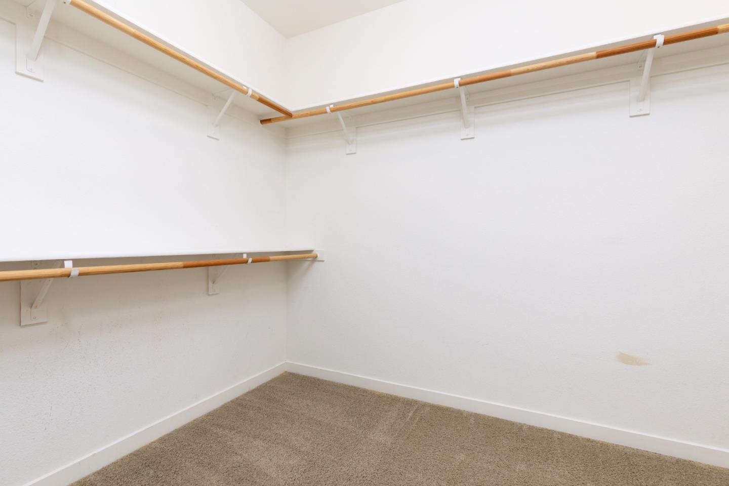 Empty walk-in closet with beige carpet and wooden clothes rods along the walls.