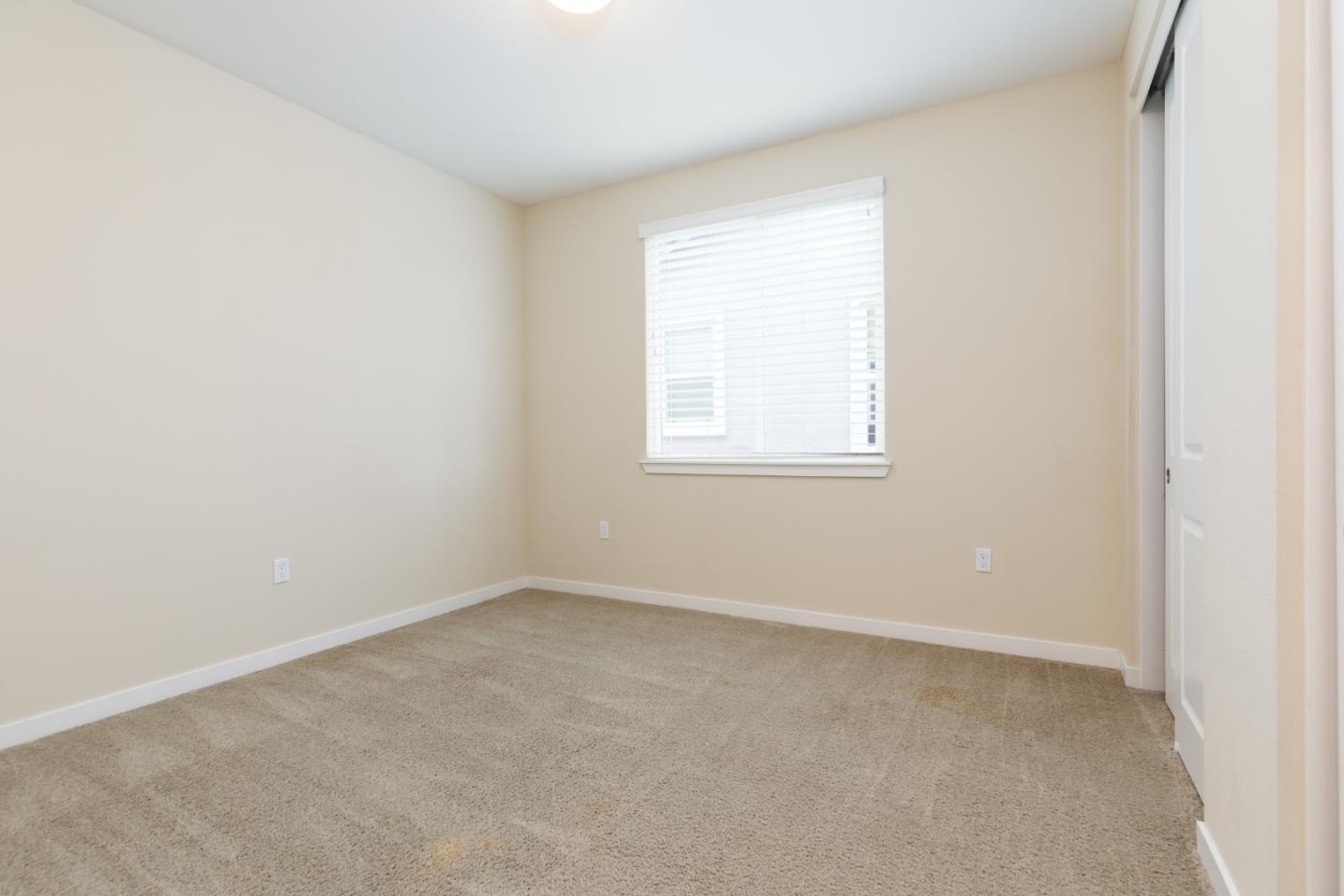 Empty bedroom with beige walls, taupe carpet, and a window with white blinds.