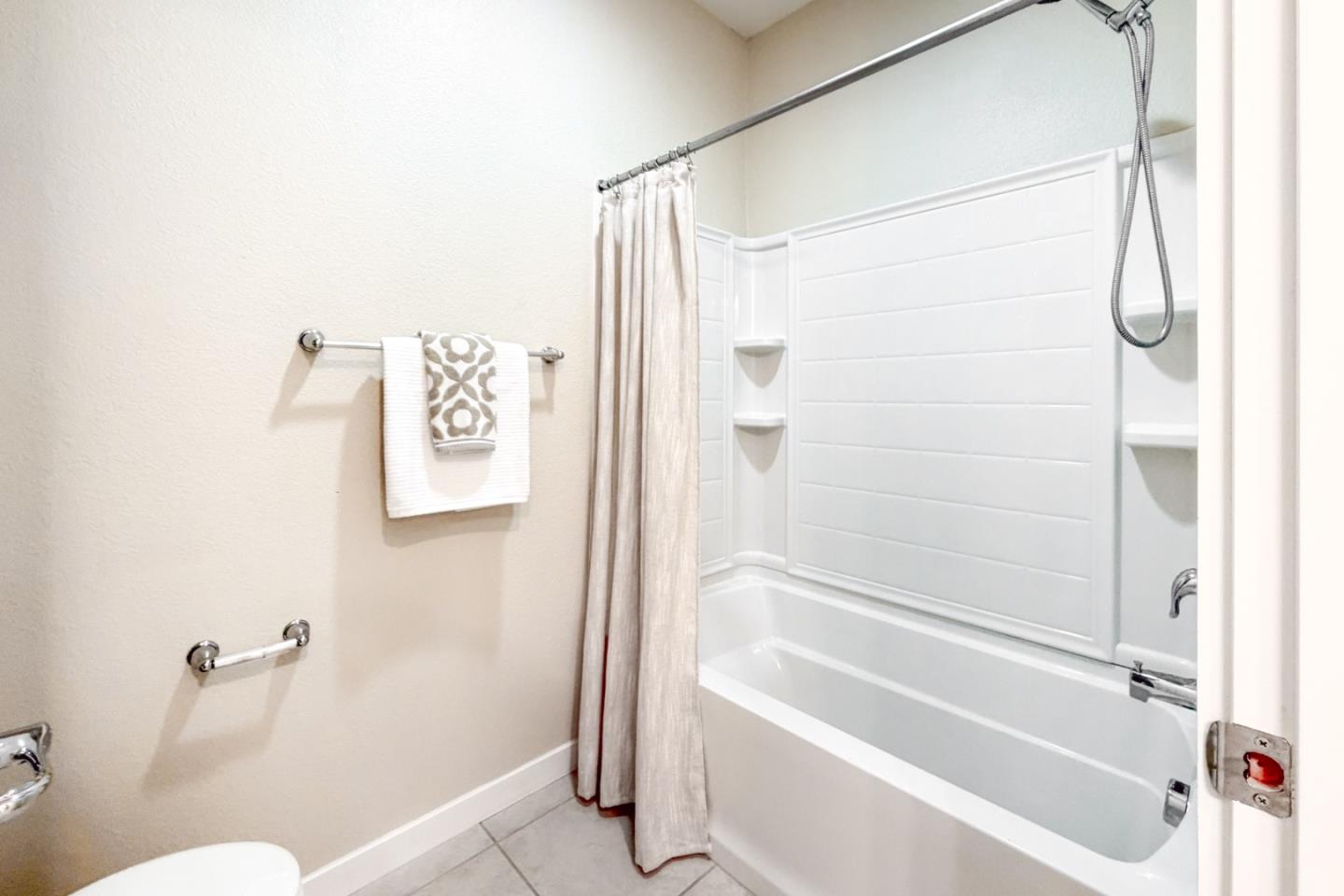 Bathroom with a white tub and shower, beige curtain, corner shelves, and towels on a wall bar.
