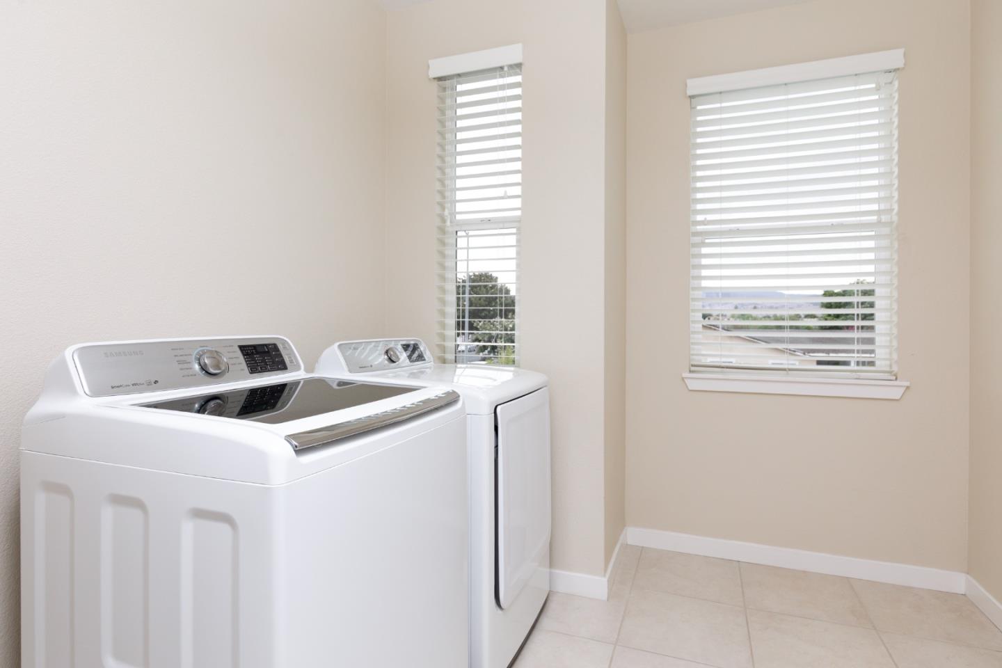 Laundry room with a white washer and dryer beside two windows with blinds.