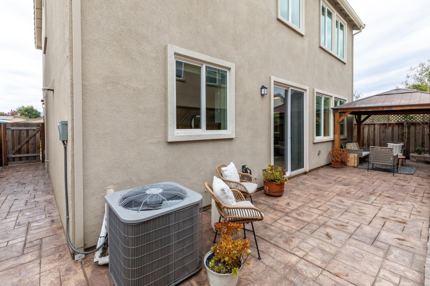 Rear patio with stamped paving, outdoor seating beneath a wooden gazebo, and sliding glass doors.