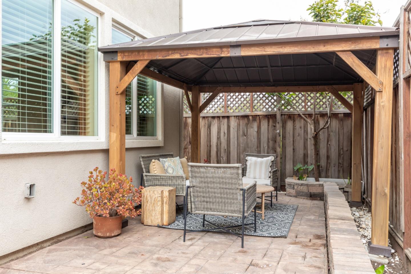 Covered backyard patio with a wood-framed gazebo, wicker seating, and paver flooring.