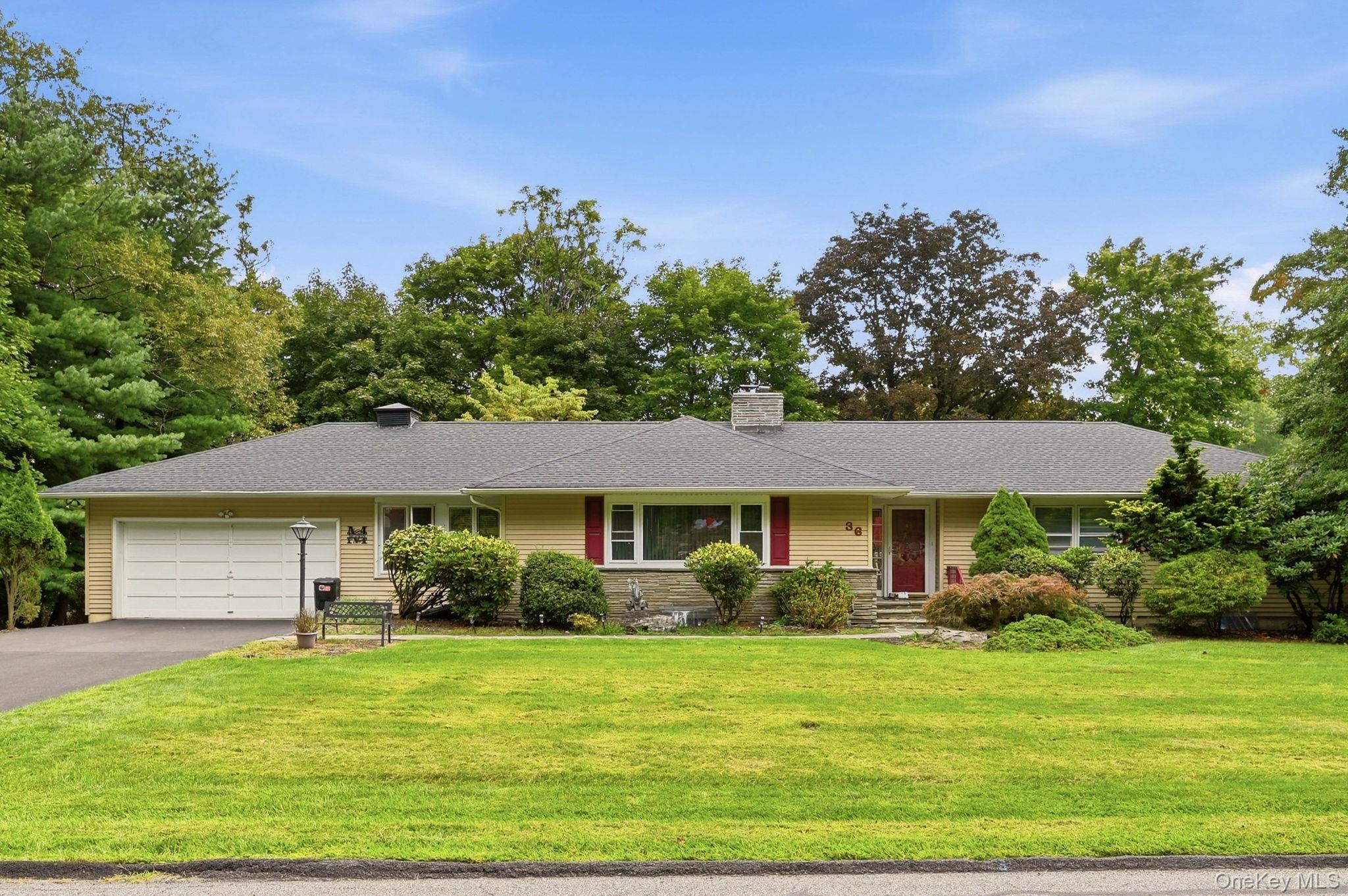 Single-story ranch home with an attached garage, red front door, and landscaped front lawn.