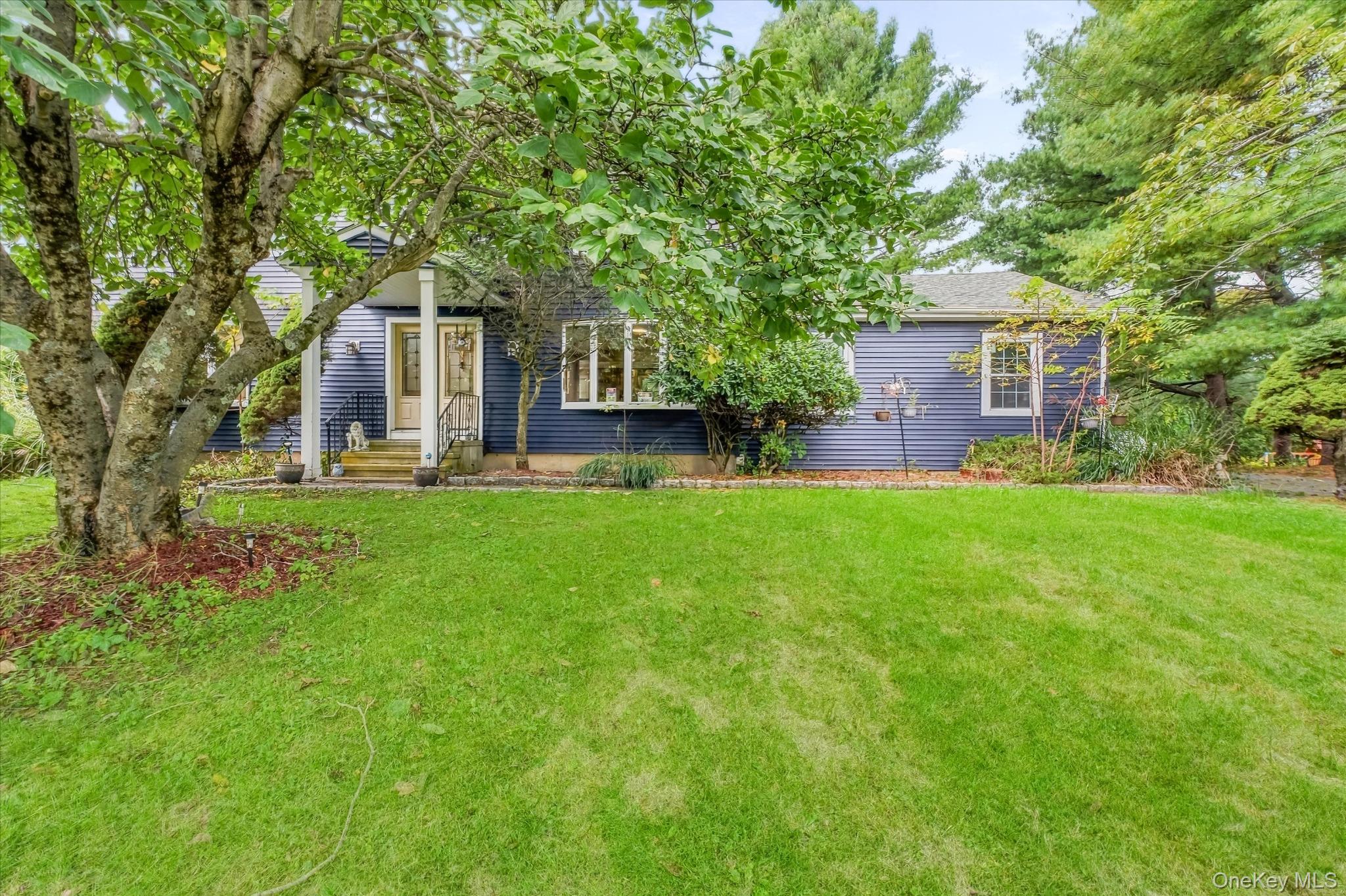 Blue-sided single-story home behind a broad lawn and mature trees.