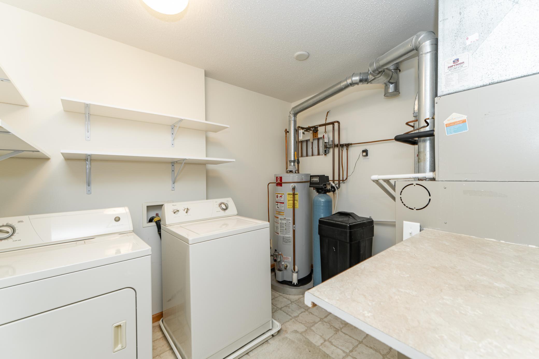 Utility room with washer and dryer, wall shelves, water heater, and furnace.
