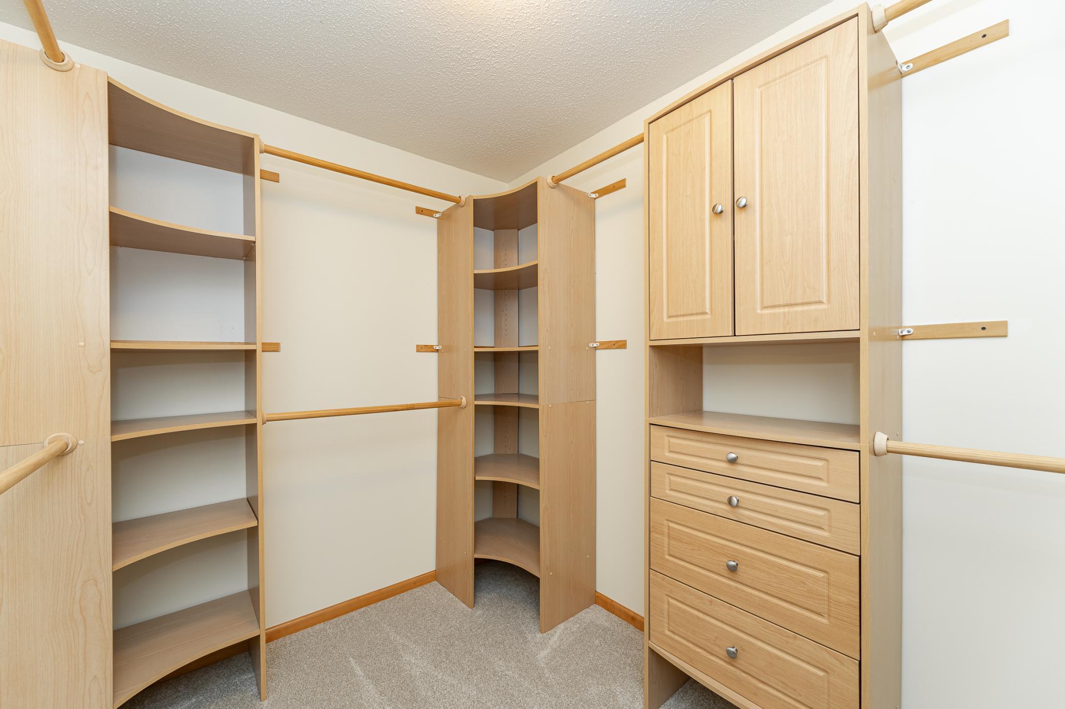 Walk-in closet with light wood shelving, hanging rods, and a built-in drawer cabinet.