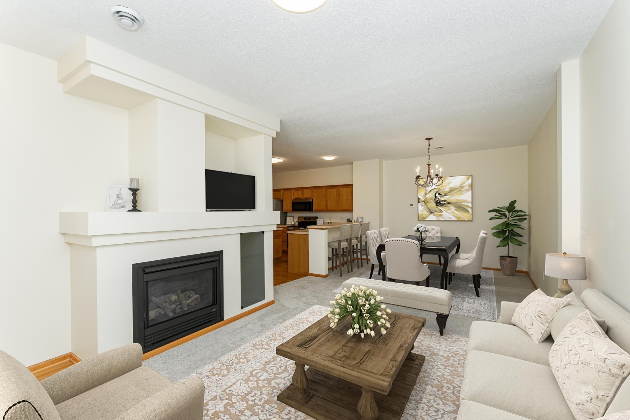 Open-plan living room with a white fireplace and mounted TV, opening to a dining area and wood-cabinet kitchen.