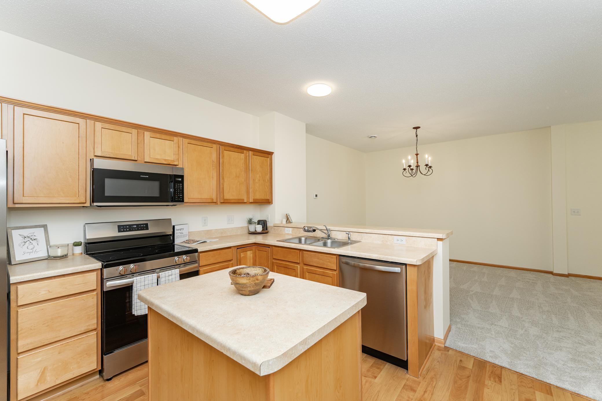 Kitchen with light wood cabinets, a central island, stainless steel appliances, and an adjoining carpeted dining area.