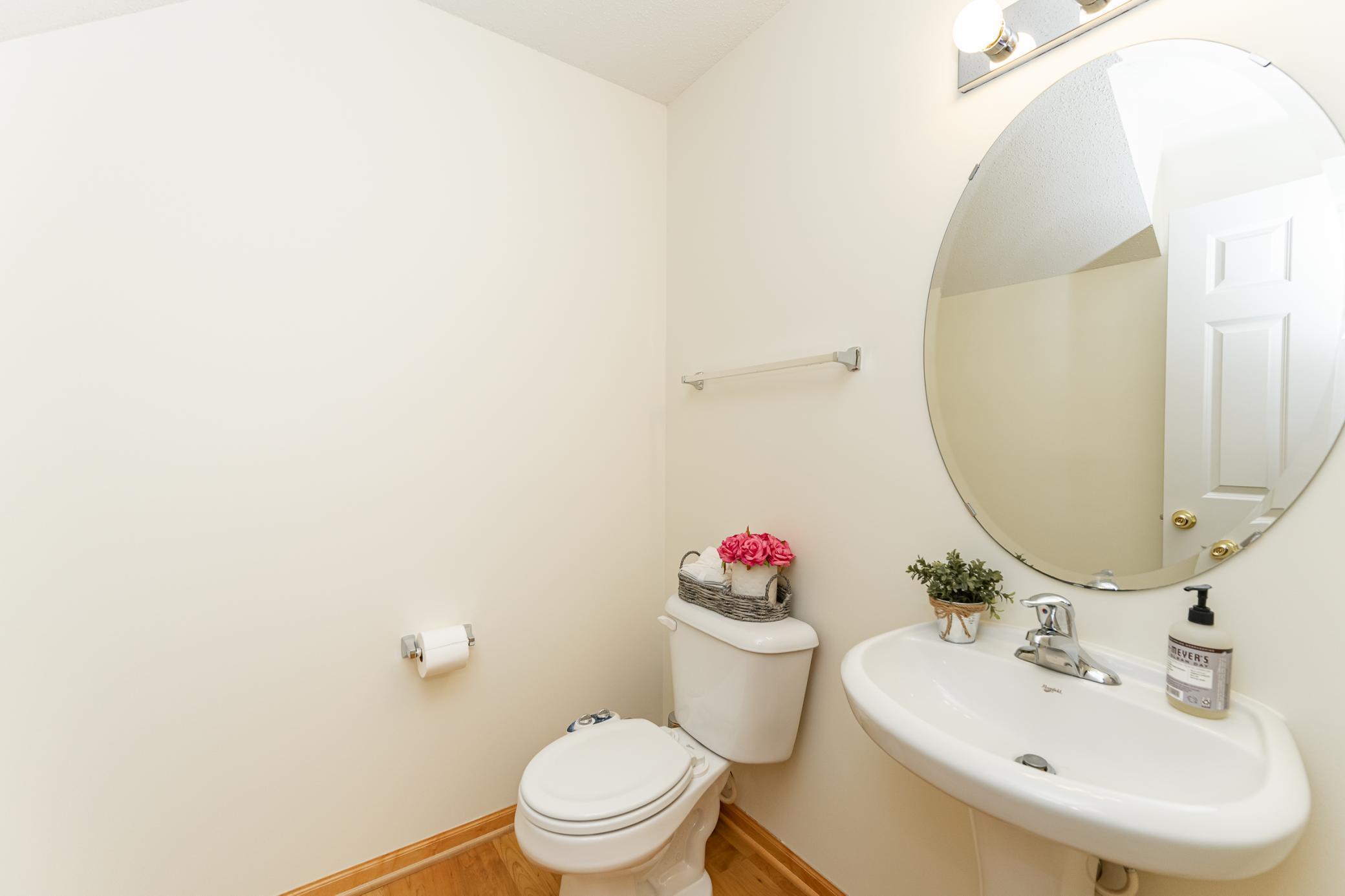 Bathroom with white toilet and pedestal sink beneath a large round mirror.