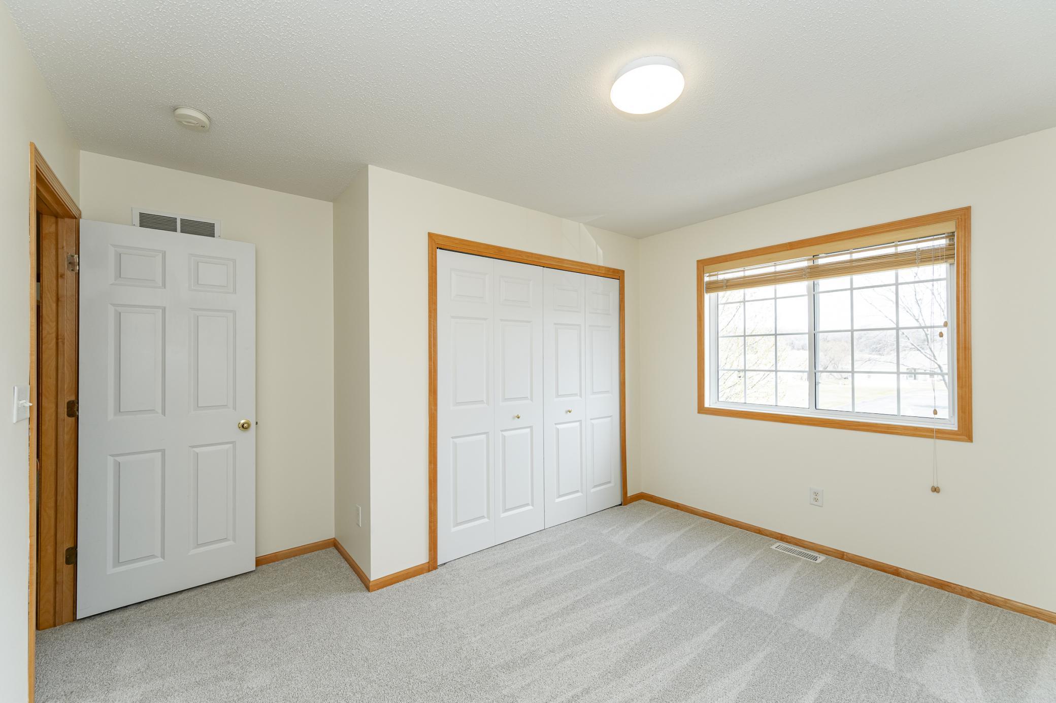 Empty bedroom with a carpeted floor, folding-door closet, and large wood-trimmed window.