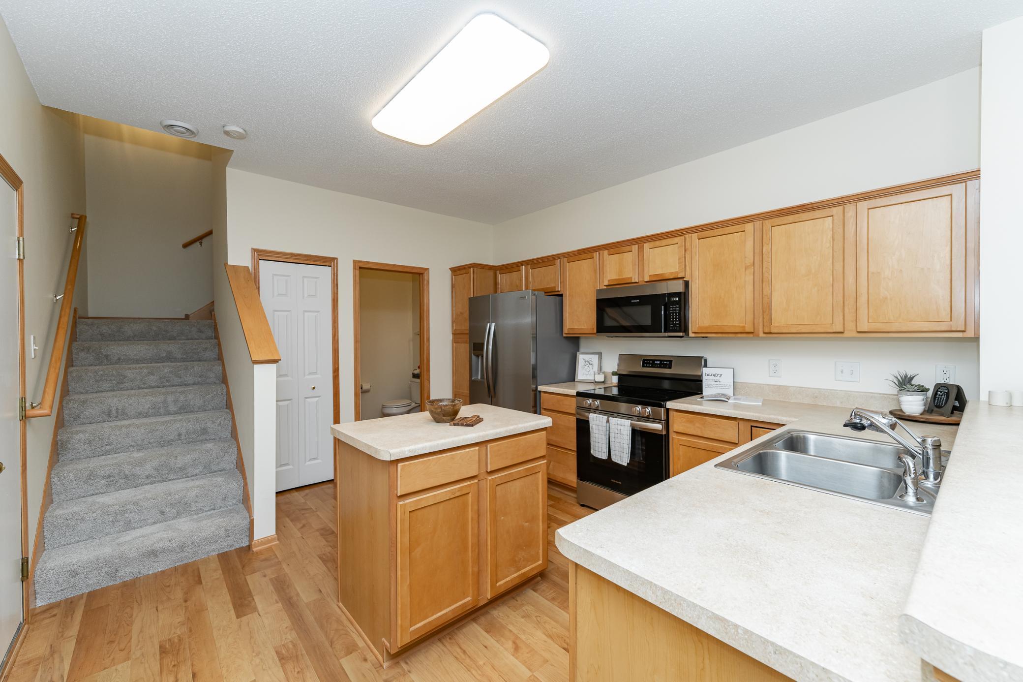 Kitchen with honey-colored cabinets, a central island, stainless steel appliances, and stairs.