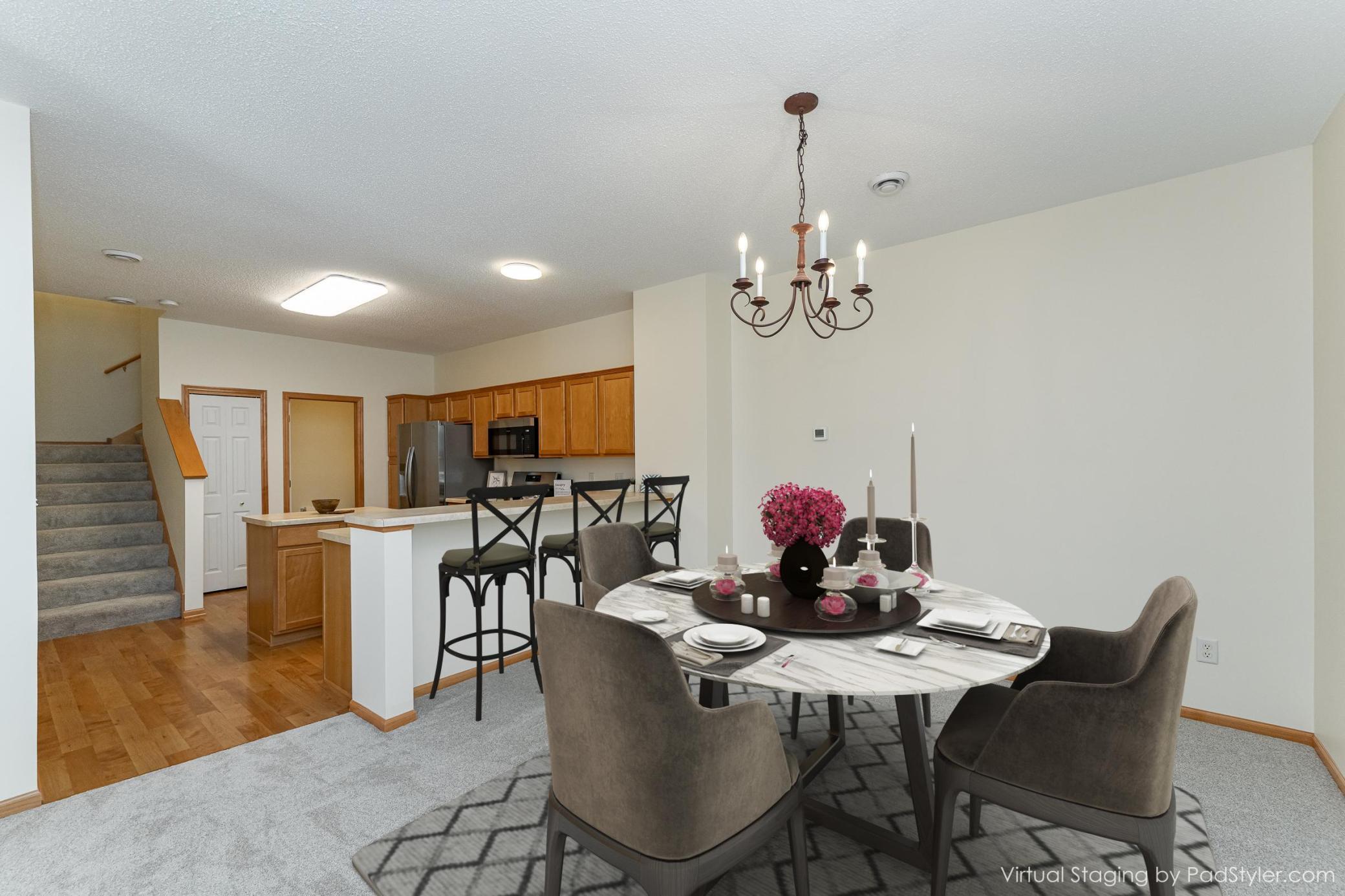Staged dining room with a marble-look table and chandelier beside an open kitchen.