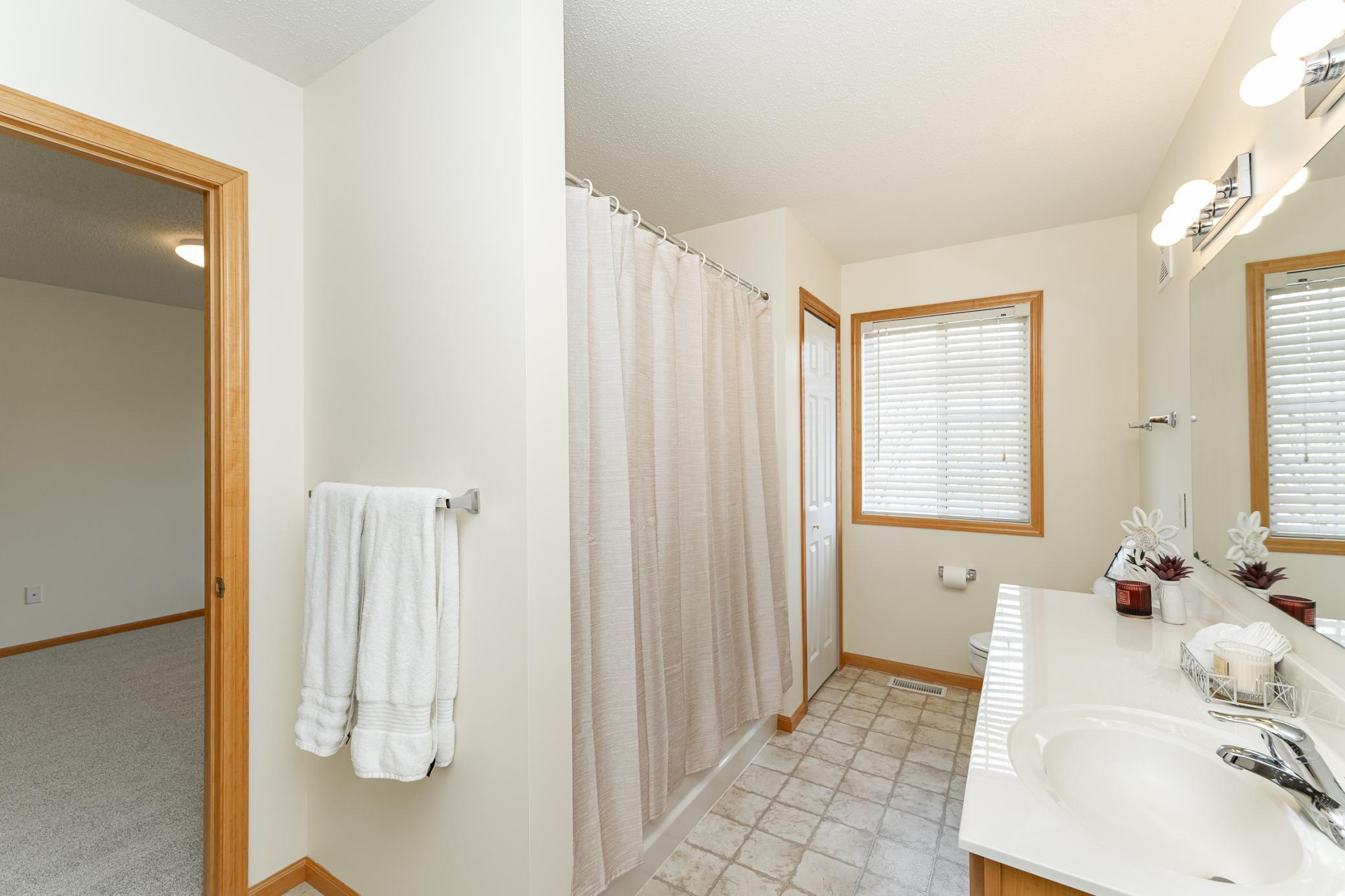 Bathroom with a tiled floor, tub and shower curtain, and long white vanity beneath a large mirror.