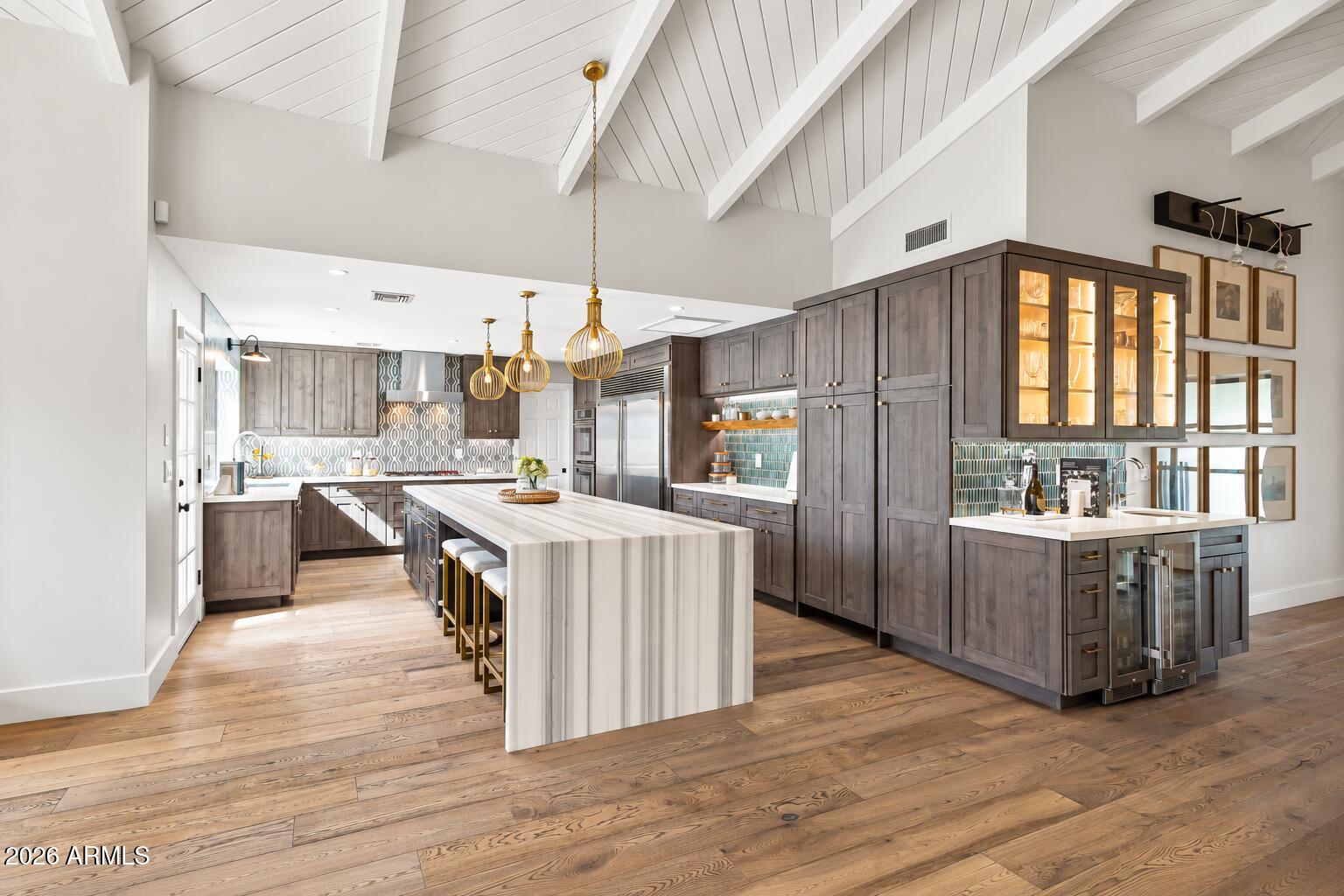 Kitchen with a large marble island, dark wood cabinets, and a high white-beamed ceiling.