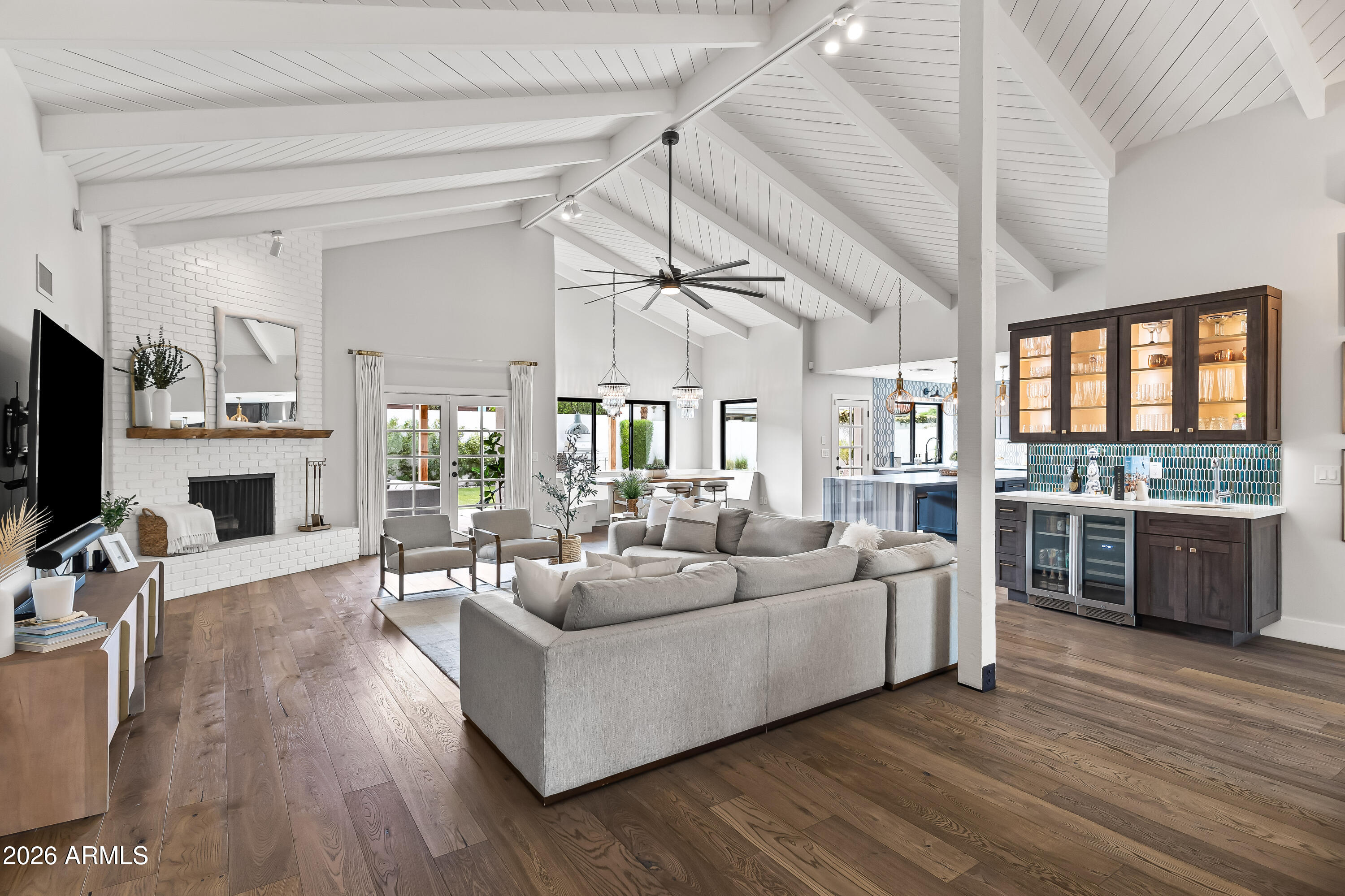 Open living room with vaulted white ceiling, brick fireplace, gray sectional, and illuminated bar cabinet.