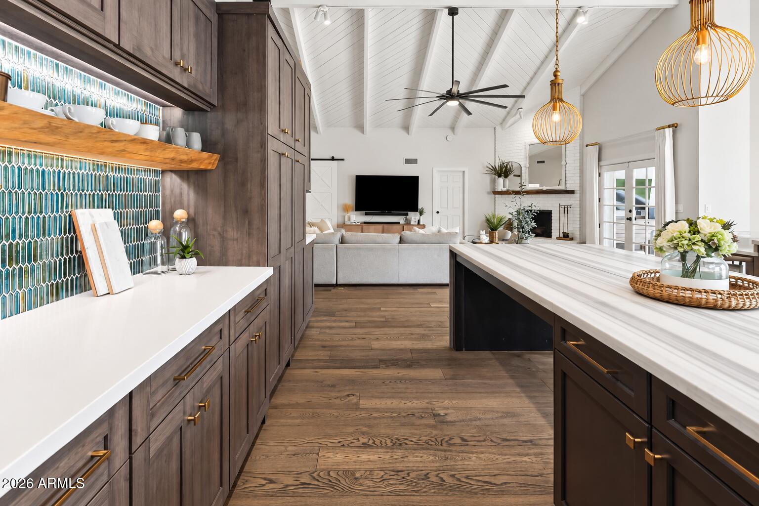 Kitchen with teal tile backsplash, dark wood cabinets, and a large island opening to a living room.