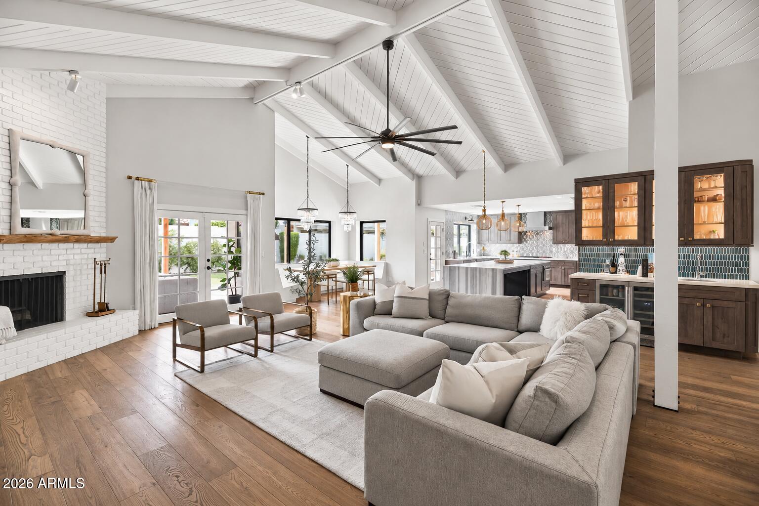 Vaulted living room with gray sectional, white brick fireplace, French doors, and open kitchen.