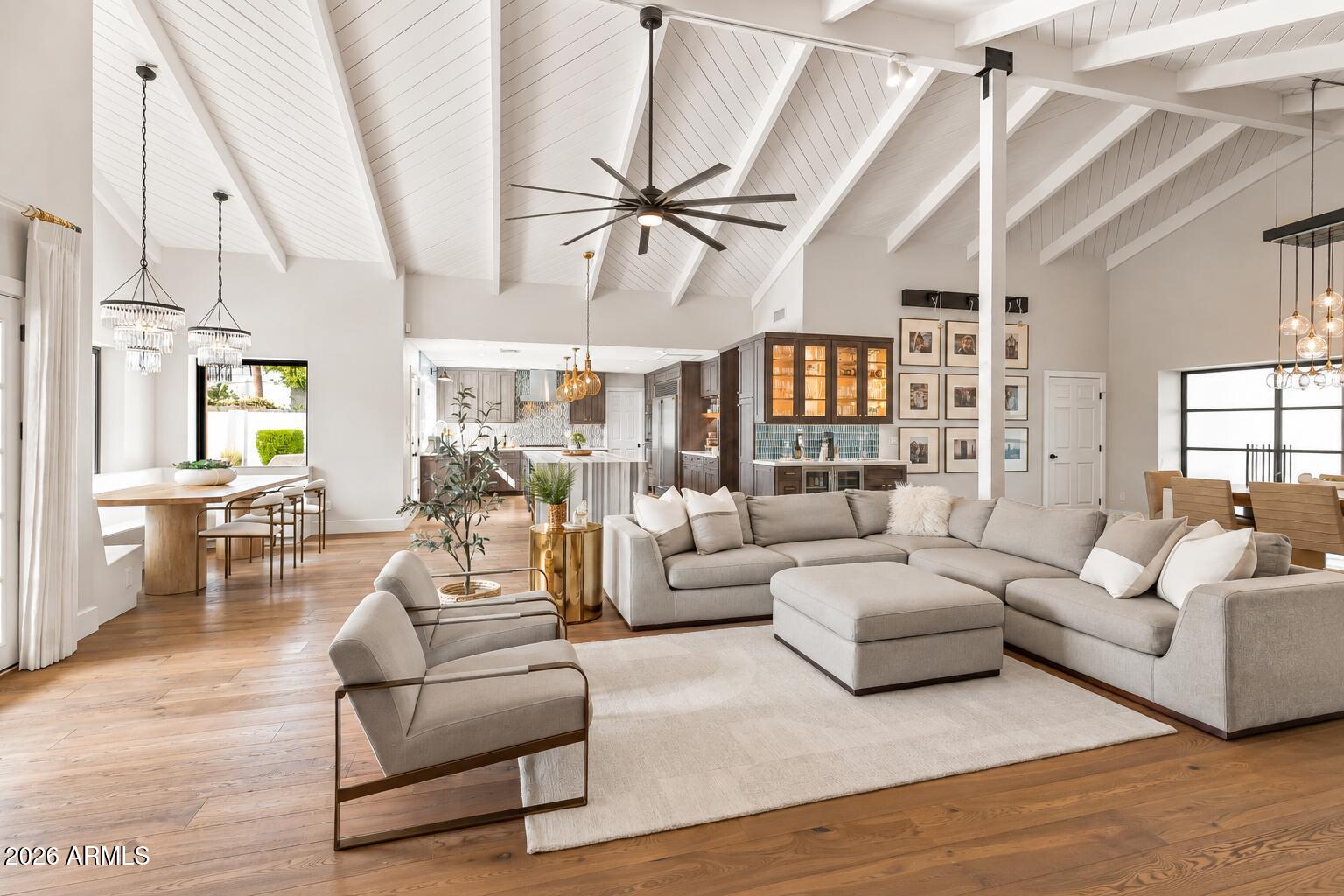 Open-plan living room with vaulted white beams, a large sectional, and adjoining kitchen and dining area.