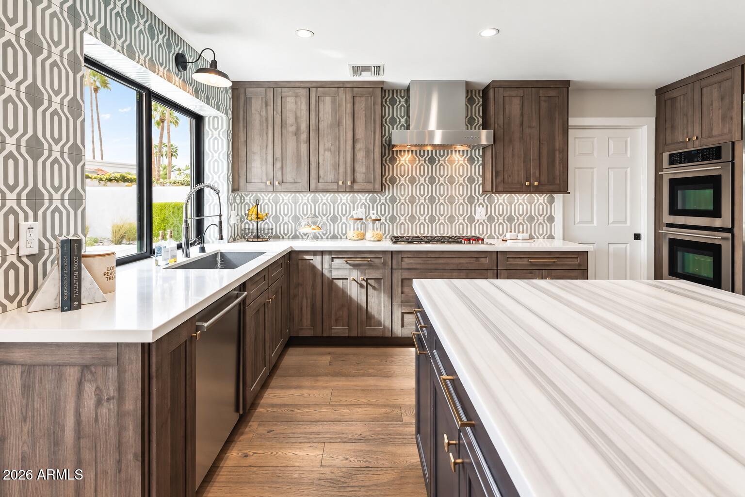 Kitchen with dark wood cabinetry, a large white island, geometric backsplash, and stainless steel appliances.