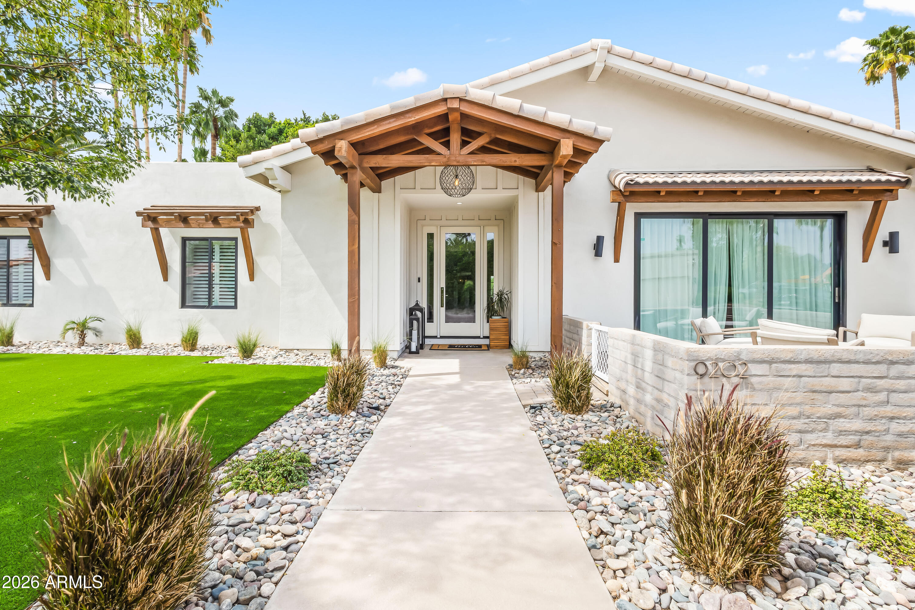 White stucco home with a timber-covered entry, stone landscaping, and a walled patio.